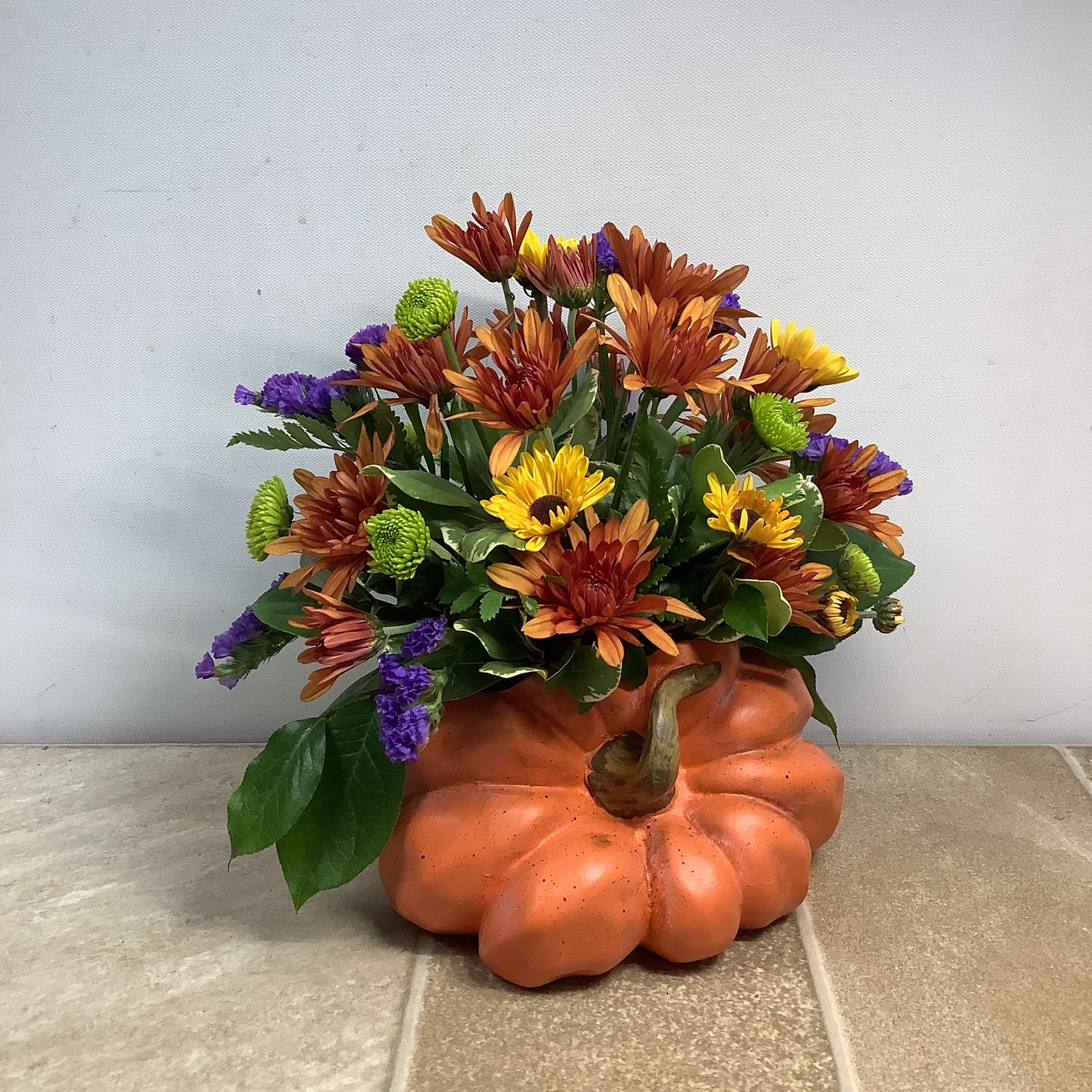 Fall flower arrangement in a pumpkin-shaped container with orange, yellow, and purple blooms