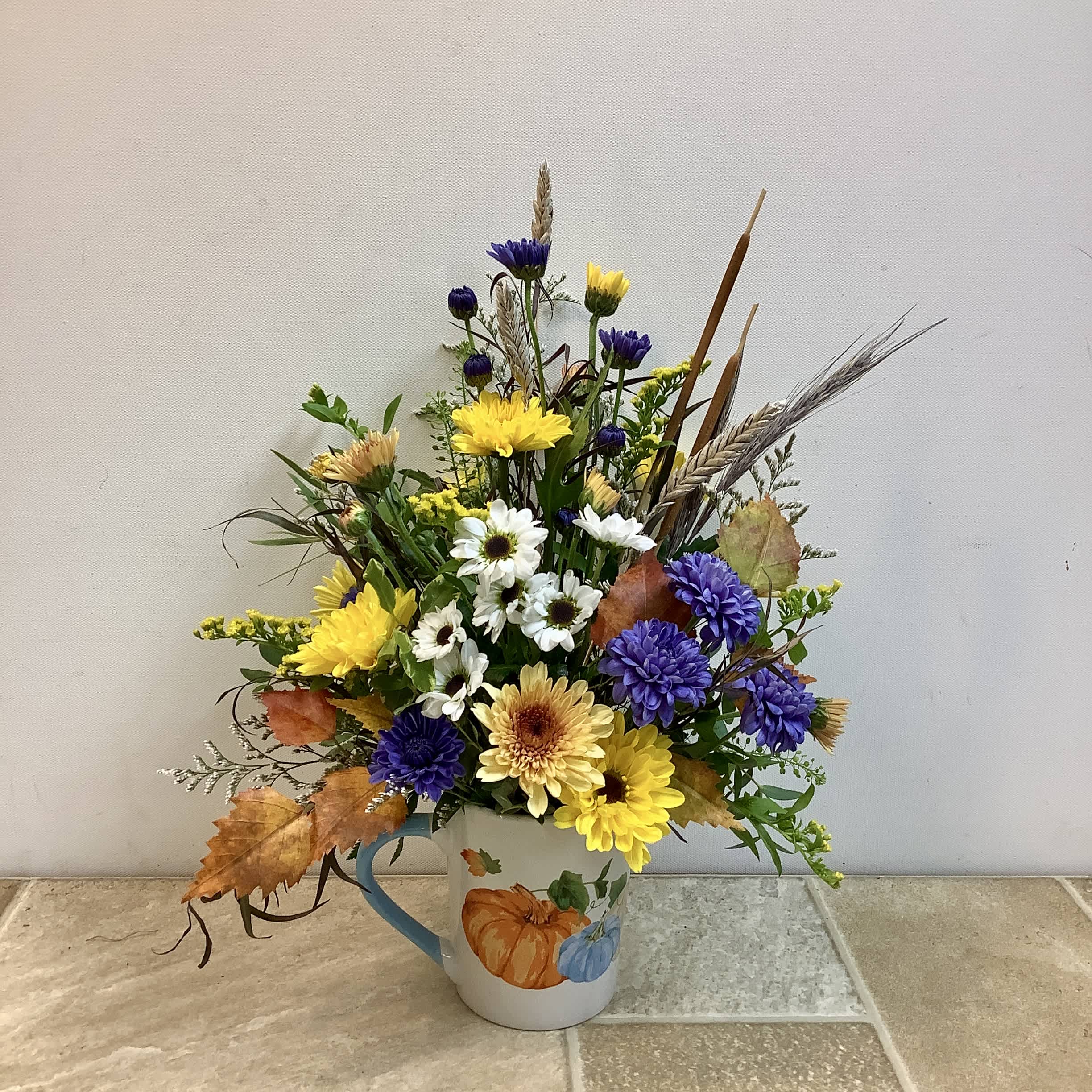 Mixed yellow, white, and purple flowers in a pumpkin mug