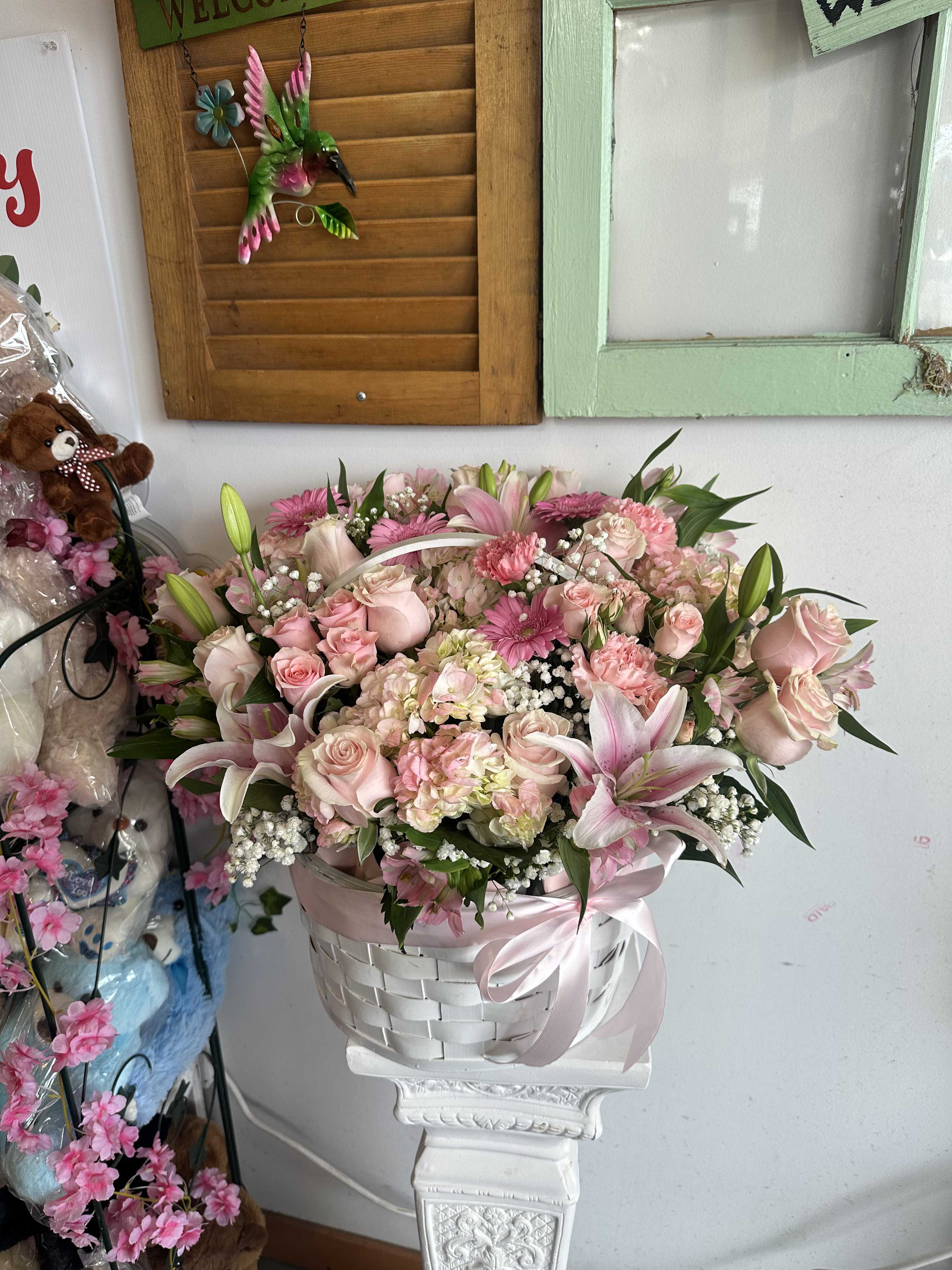 Pink floral arrangement in a white basket with a satin ribbon