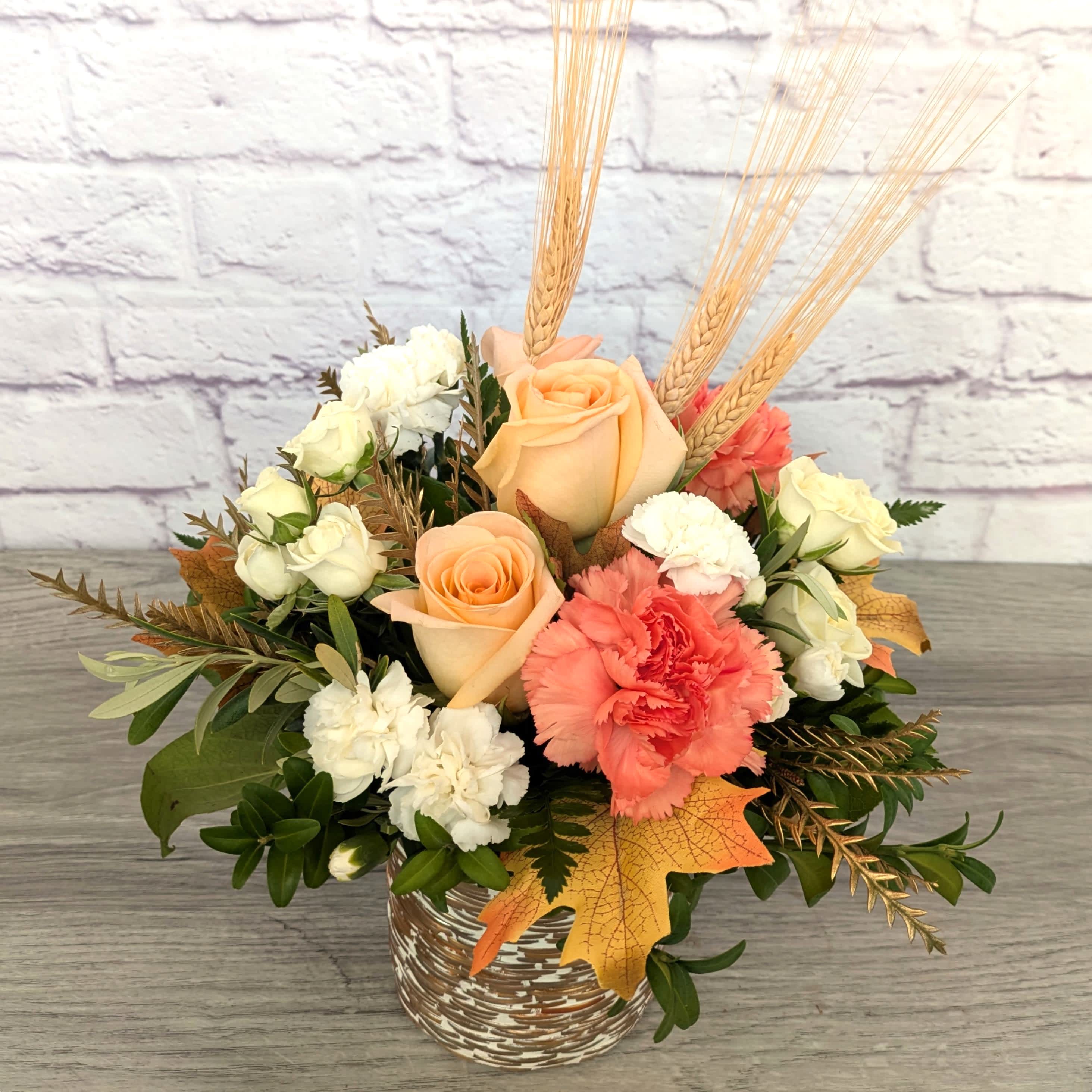 Peach roses and white carnations in a woven vase with wheat accents