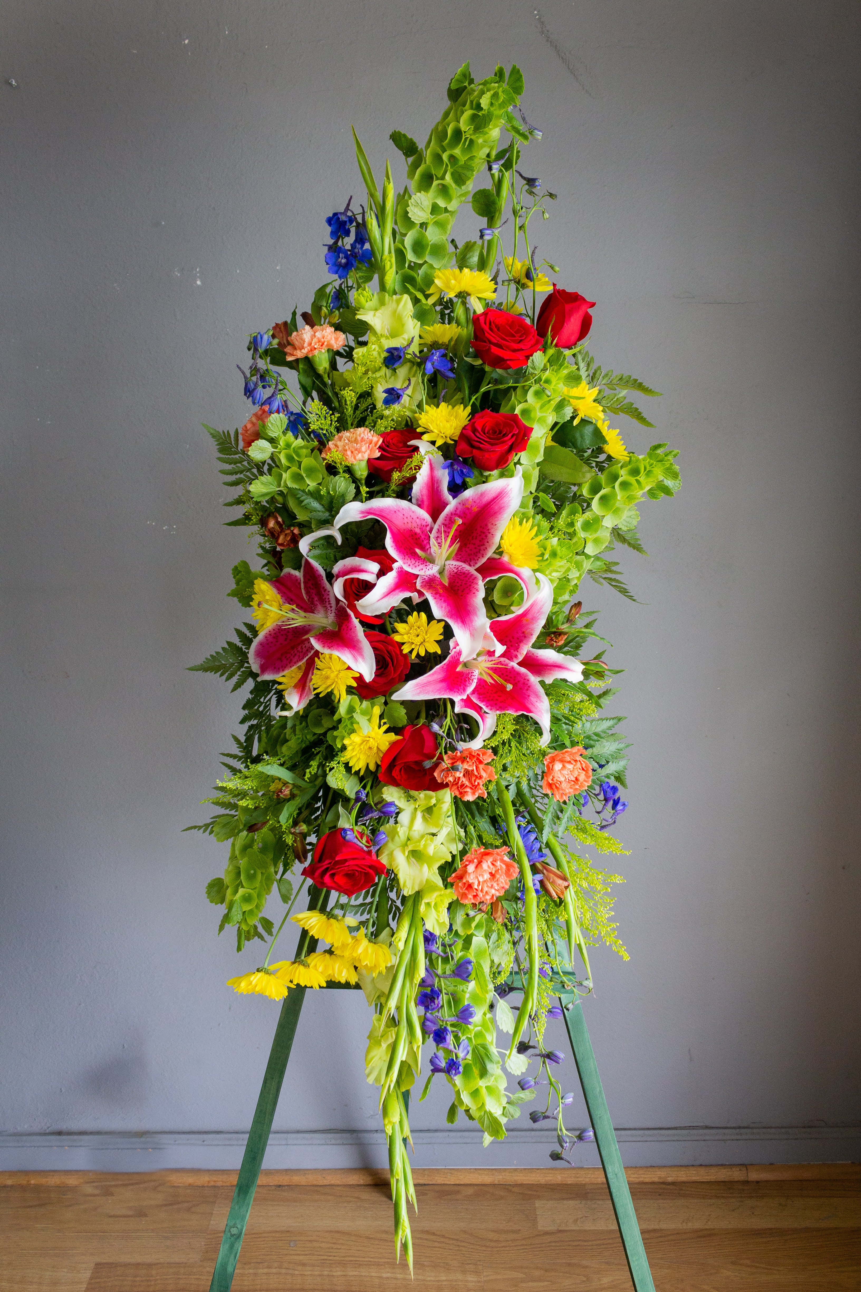 Tall standing floral spray with pink lilies, red roses, and bright mixed blooms