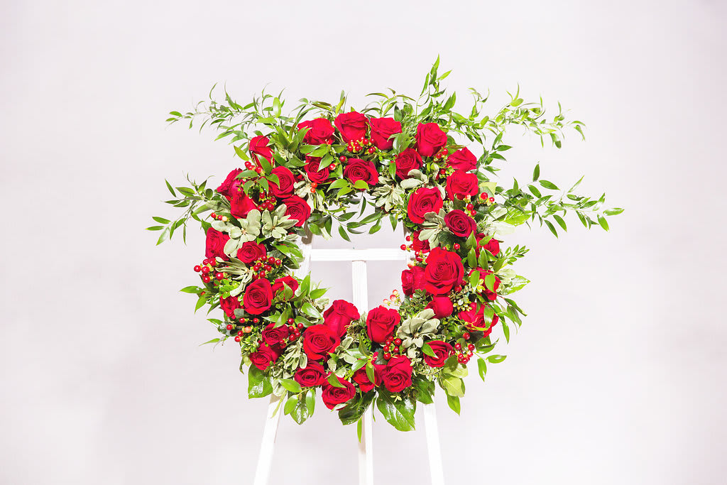 Heart-shaped wreath of red roses and greenery on a white stand