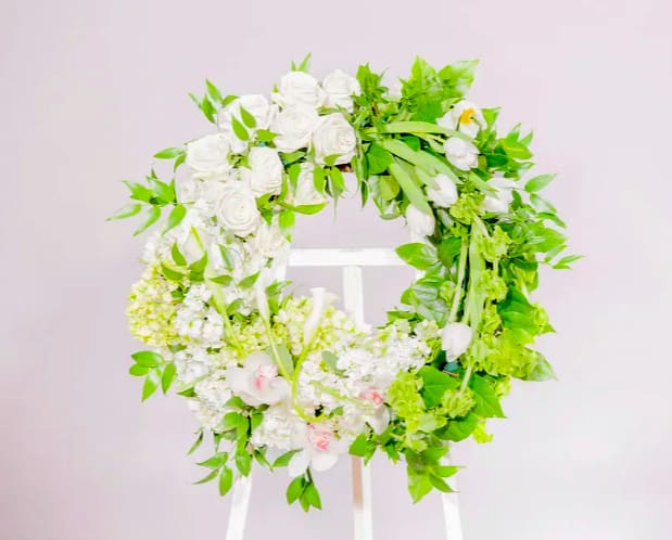 White floral wreath with green foliage on a stand