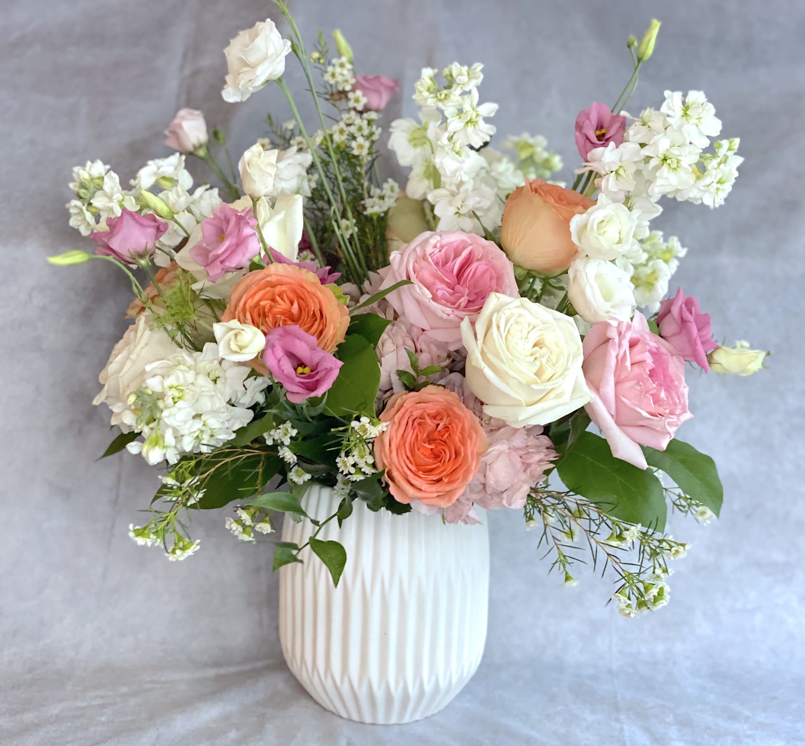 Pink, peach, and white flowers arranged in a white vase