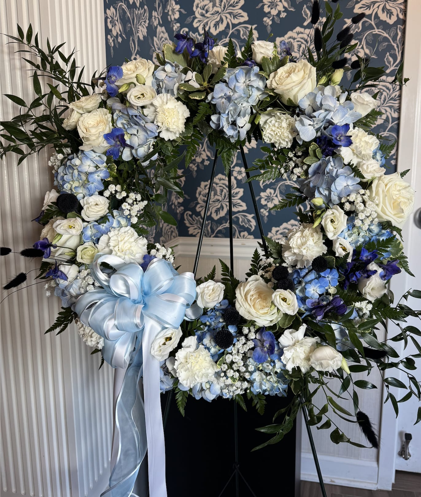 Large floral wreath with white and blue flowers and a pale blue ribbon bow