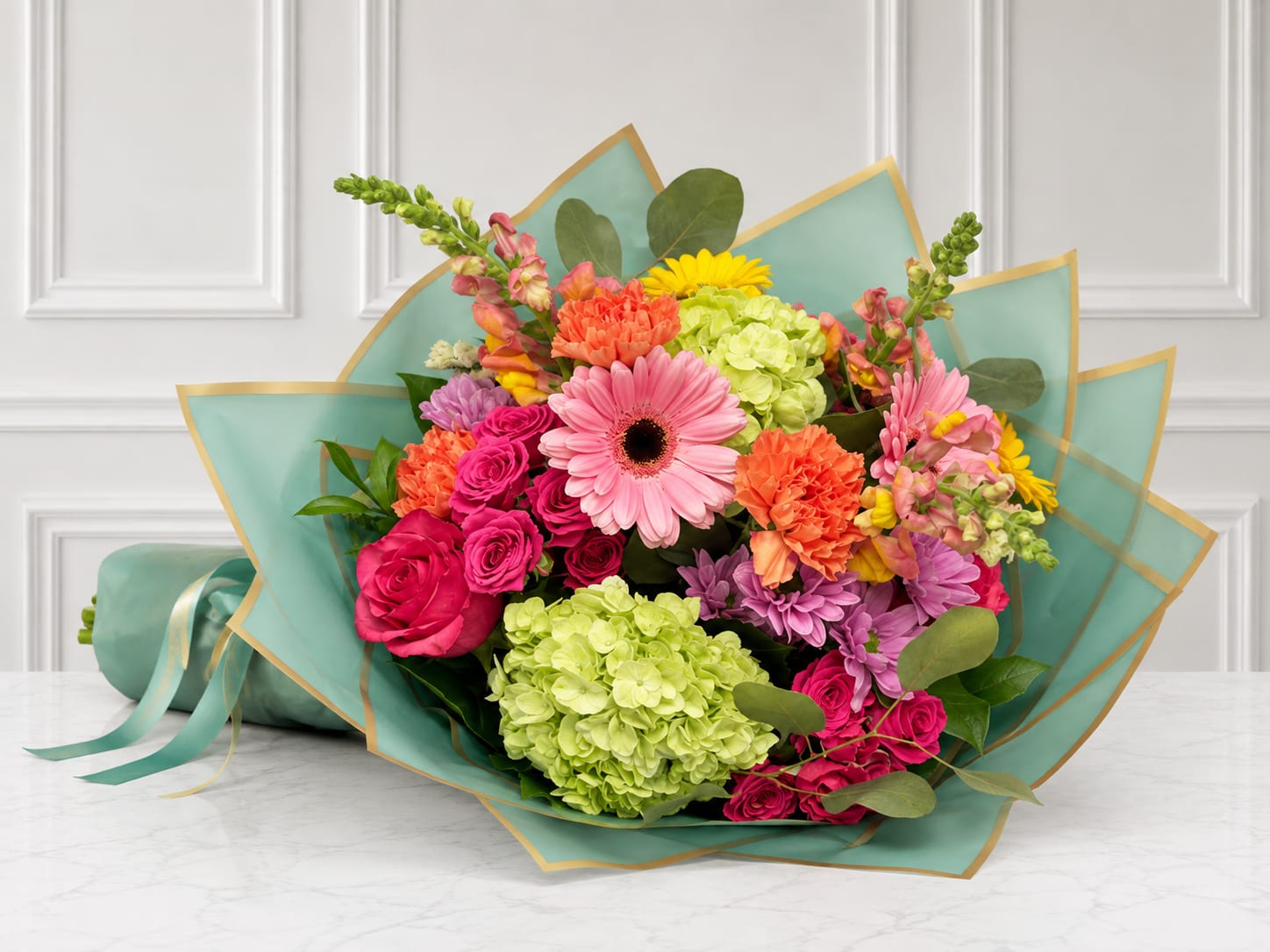Mixed bouquet of pink, orange, yellow, and green flowers wrapped in teal paper