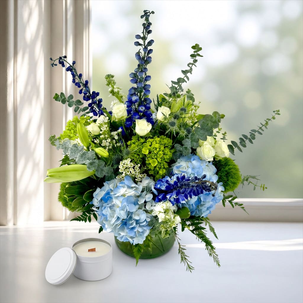 Blue and white floral arrangement in a green vase with a white candle nearby