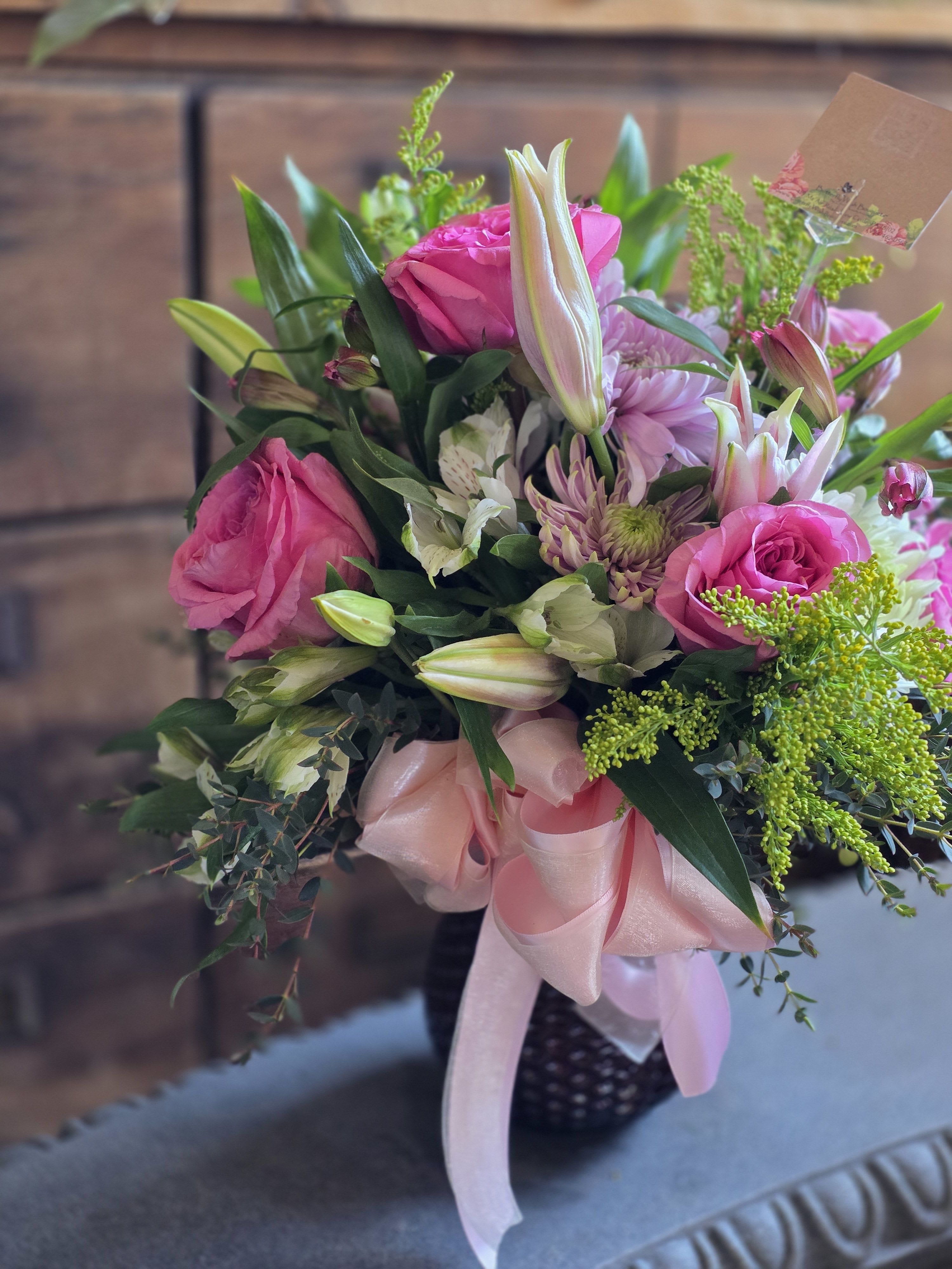The Blushing Belle - Soft, sweet, and perfectly radiant, The Blushing Belle is a cheerful departure from the traditional red rose bouquet. This garden-inspired arrangement features a romantic dance of velvety pink roses and majestic white lilies, layered with long-lasting pink alstroemeria and fluffy white mums.  For a unique "Butterfly" touch, we’ve accented these soft tones with pops of airy yellow solidago, adding a hint of sunshine to the winter season. Artfully arranged in a lovely glass vase and finished with a festive Valentine’s Day bow, it’s a gift that looks as beautiful as it smells!  The Look: Classic romance with a bright, cheerful twist.  The Details: Includes roses, lilies, alstroemeria, mums, and solidago in a designer vase.  Perfect For: The person who brings a little extra sunshine into your life.  Bring home a little extra charm this Valentine’s Day—order The Blushing Belle today!