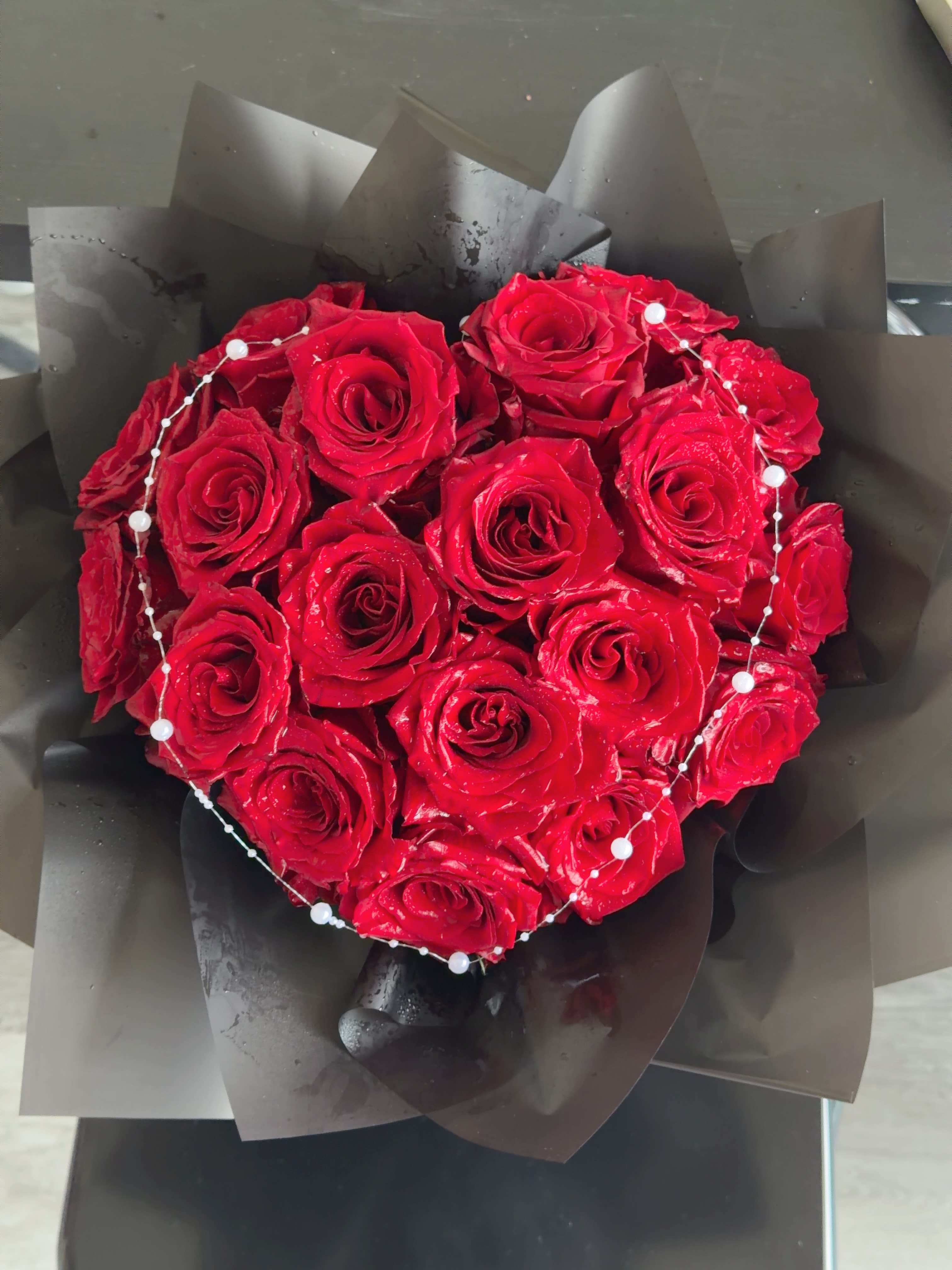 Heart-shaped bouquet of red roses wrapped in black paper with pearl accents
