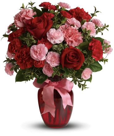 Red roses and red and pink carnations in a red glass vase with a pink bow