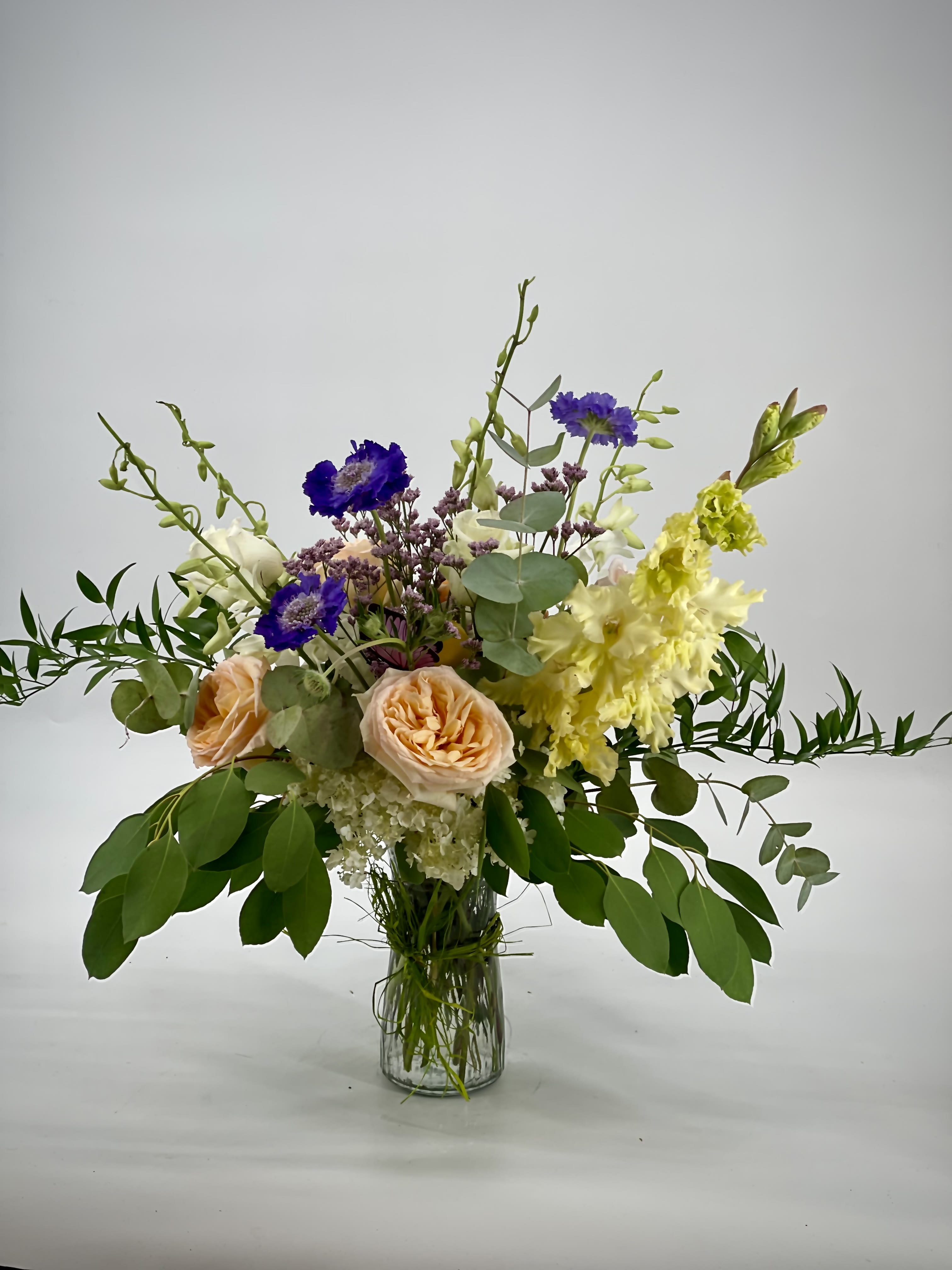 Mixed bouquet in a clear glass vase with peach roses and purple blooms