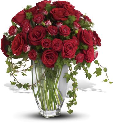 Red roses arranged in a clear glass vase with trailing greenery