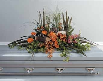 Orange floral casket spray with tall grasses and greenery