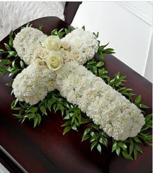White floral cross arrangement on a dark casket