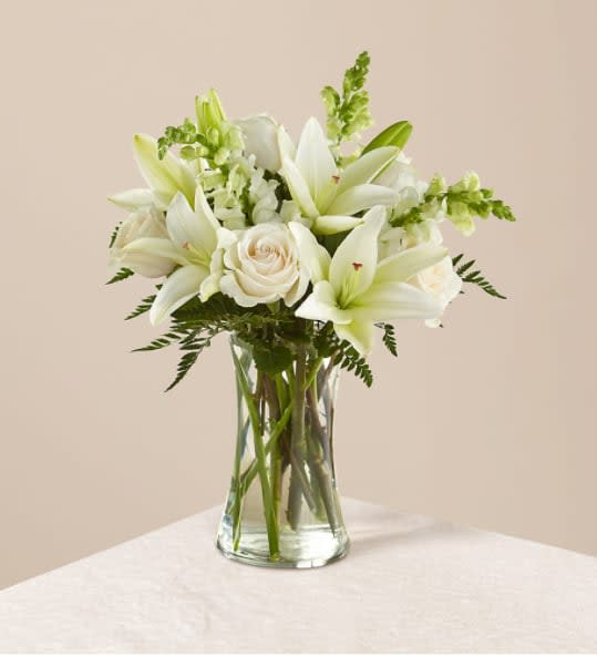 Eternal Friendship Bouquet - An exuberance of bright and beautiful white blossoms provides an exquisite way to deliver your expressions of sympathy and comfort. This life affirming tribute combines white roses, snapdragons and Asiatic lilies accented by lush greens arranged in a clear glass 8" vase. An excellent choice for a wake, funeral service or for sending your condolences to the home of grieving family or friends.