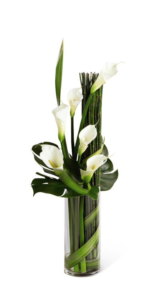 White calla lilies arranged in a tall glass vase with bamboo