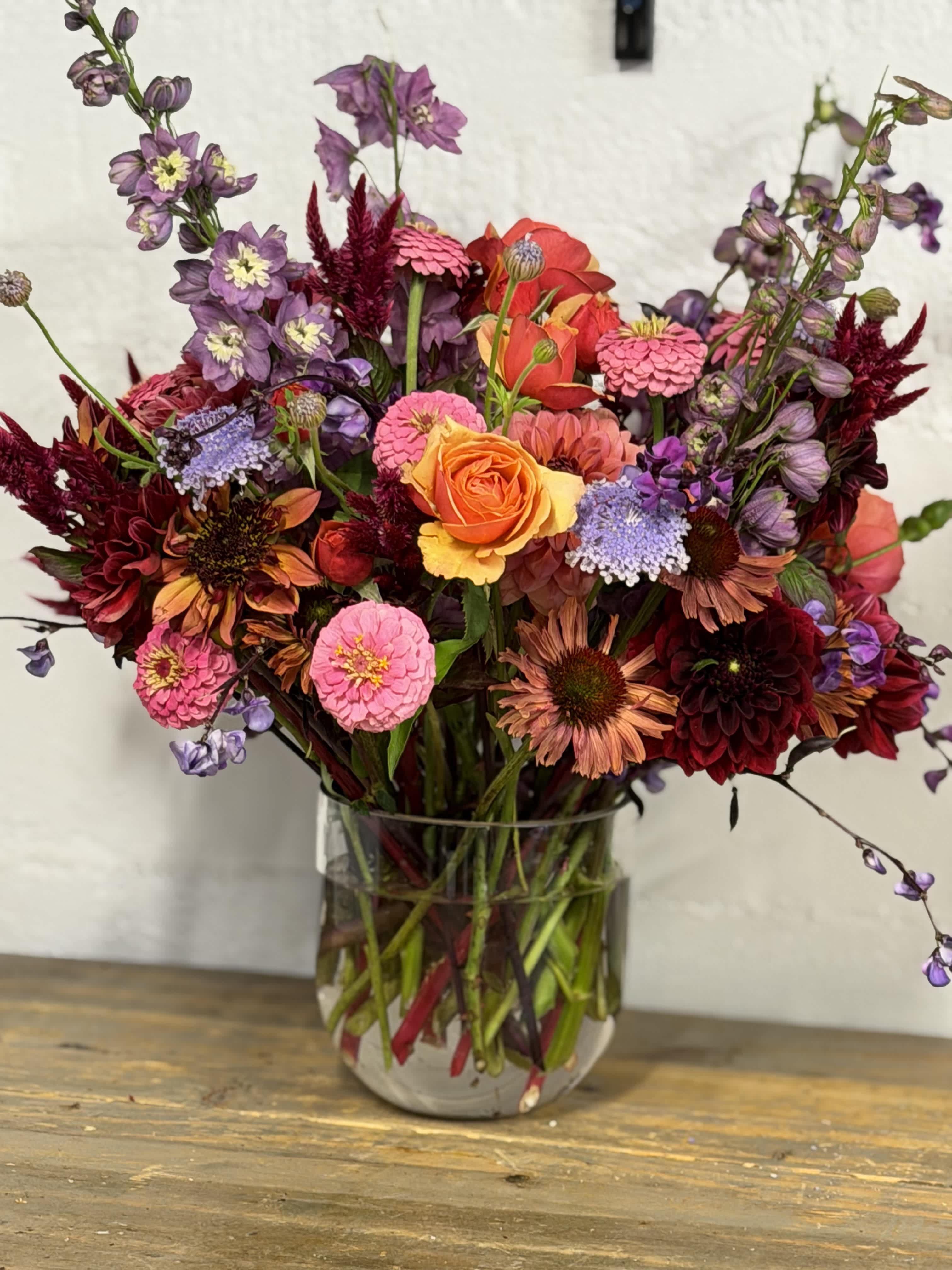 Mixed bouquet of orange, pink, purple, and burgundy flowers in a glass vase