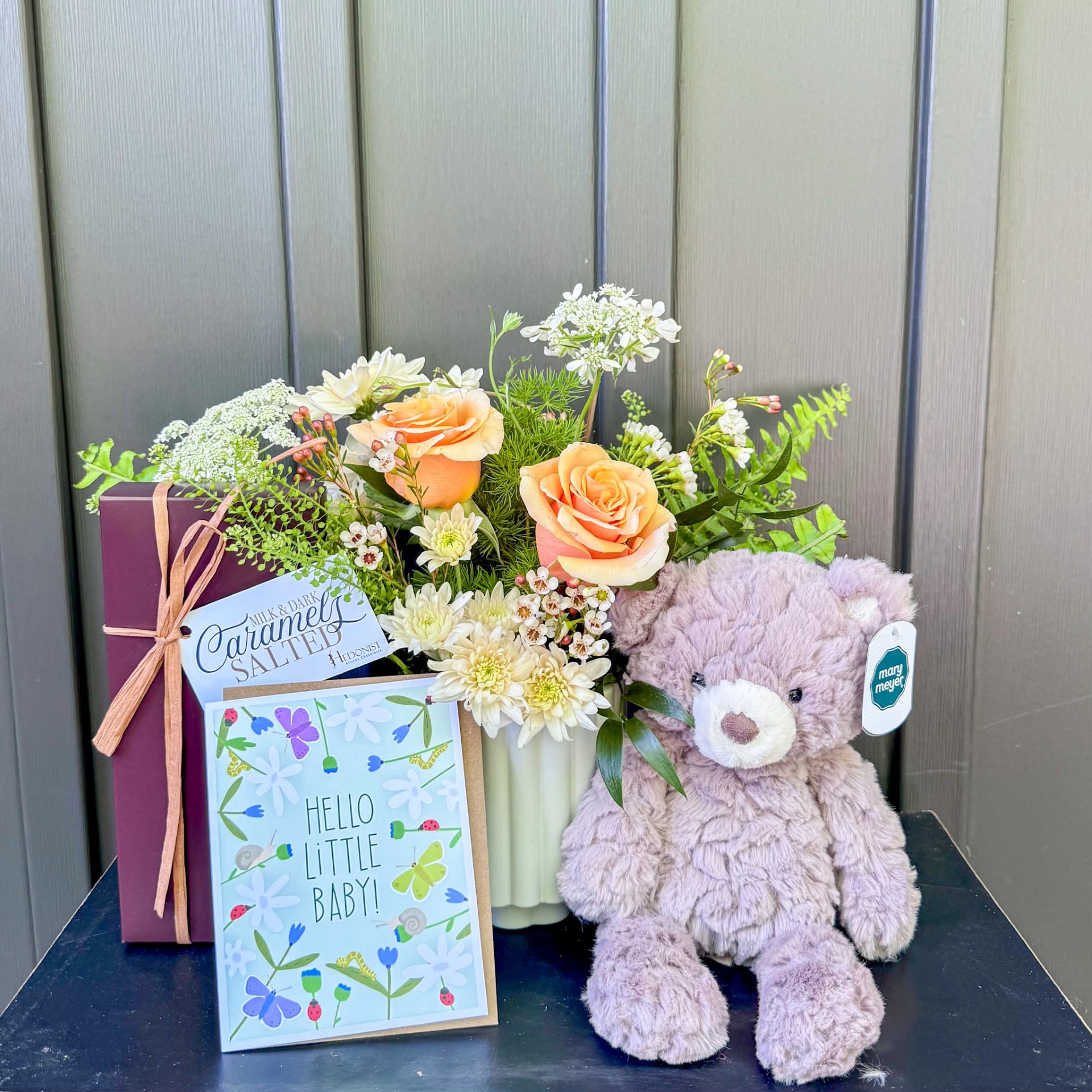 Little One Gift Set - Curated to celebrate a little one and their family! This gift set includes an irresistibly cuddly stuffed bear, locally made Hedonist caramels, and a stunning seasonal flower arrangement. Flower colors can be customized in our notes section in checkout. Upgrade to deluxe and premium for a larger floral arrangement.  If a flower pictured is unavailable for any reason, we will substitute for a flower of the same or higher value and in a similar style and color.