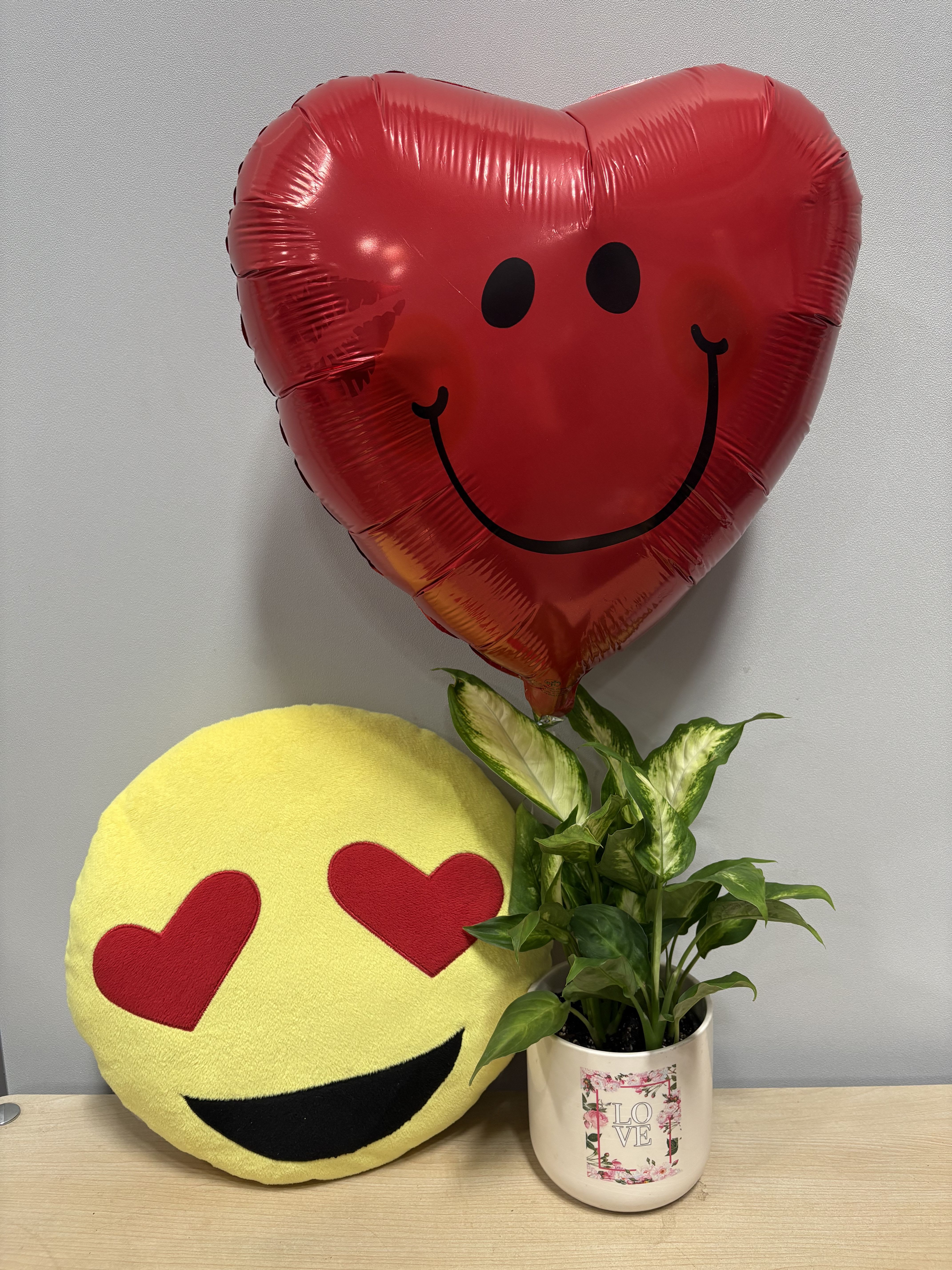 Heart-shaped red balloon, emoji pillow, and potted plant in a decorative mug