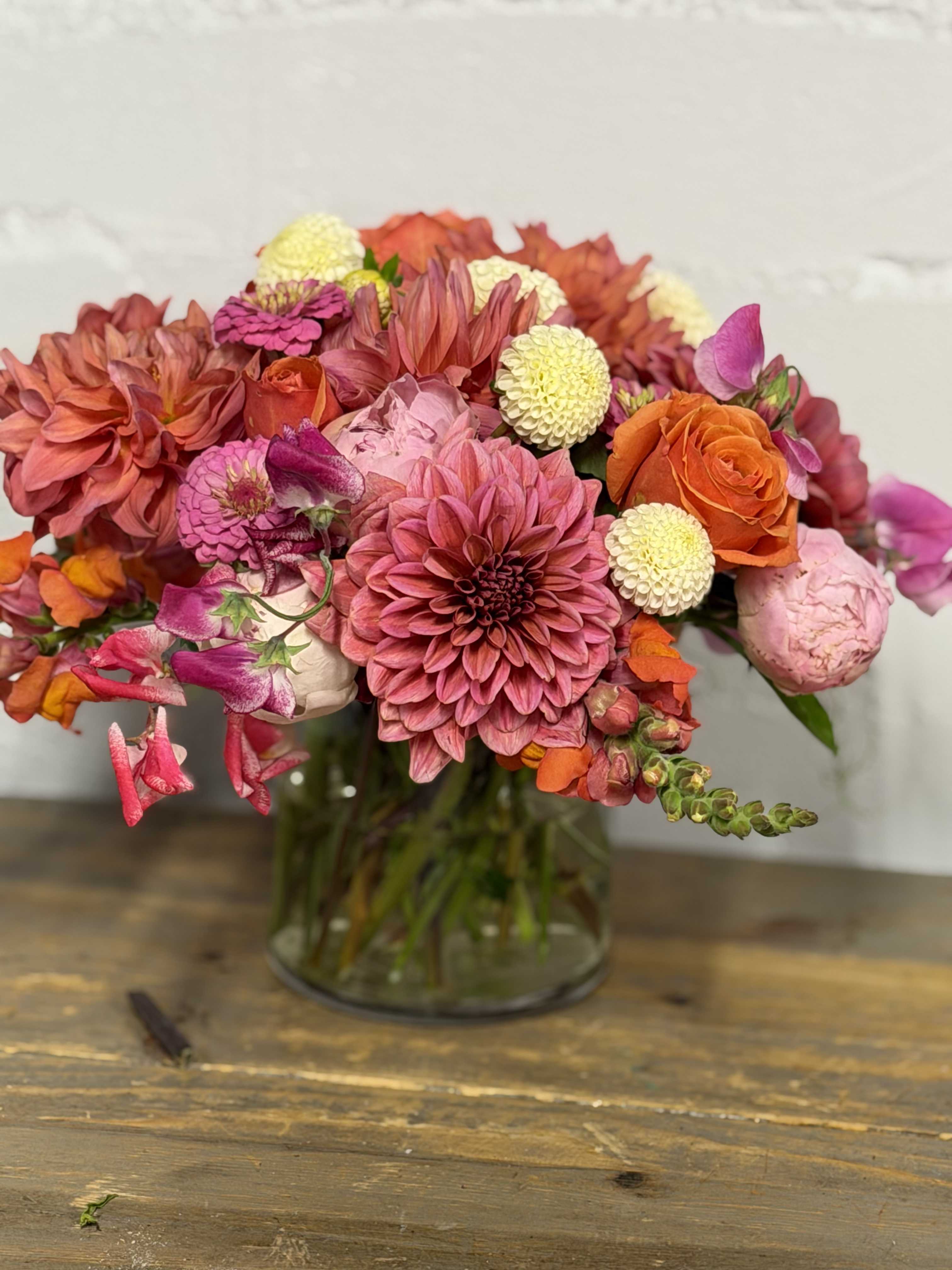Mixed bouquet of pink, orange, and cream flowers in a glass vase