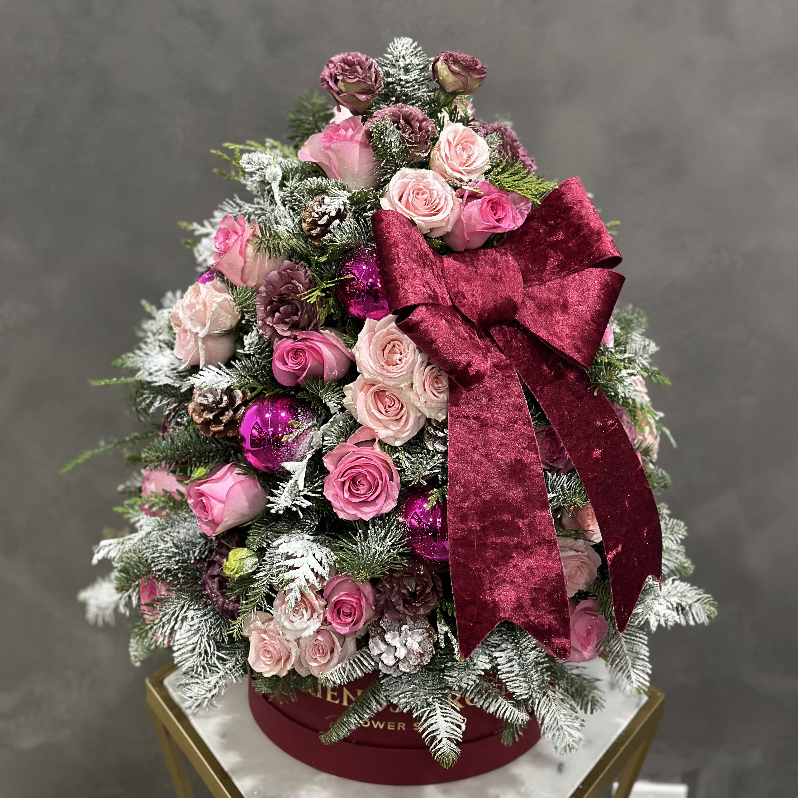 Pink roses arranged like a Christmas tree with a burgundy bow and ornaments