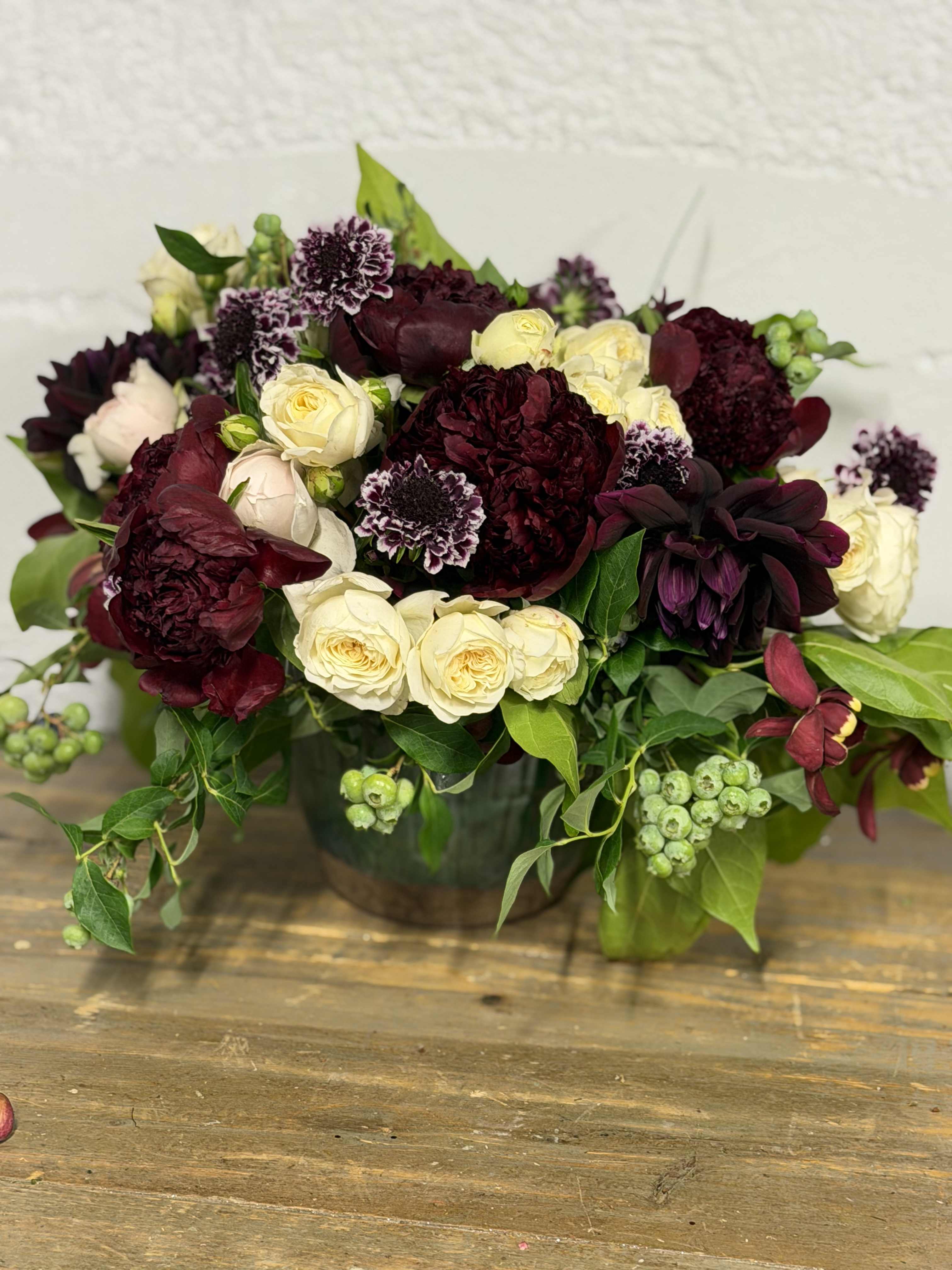 Bouquet of burgundy and cream roses with dark blooms in a vase