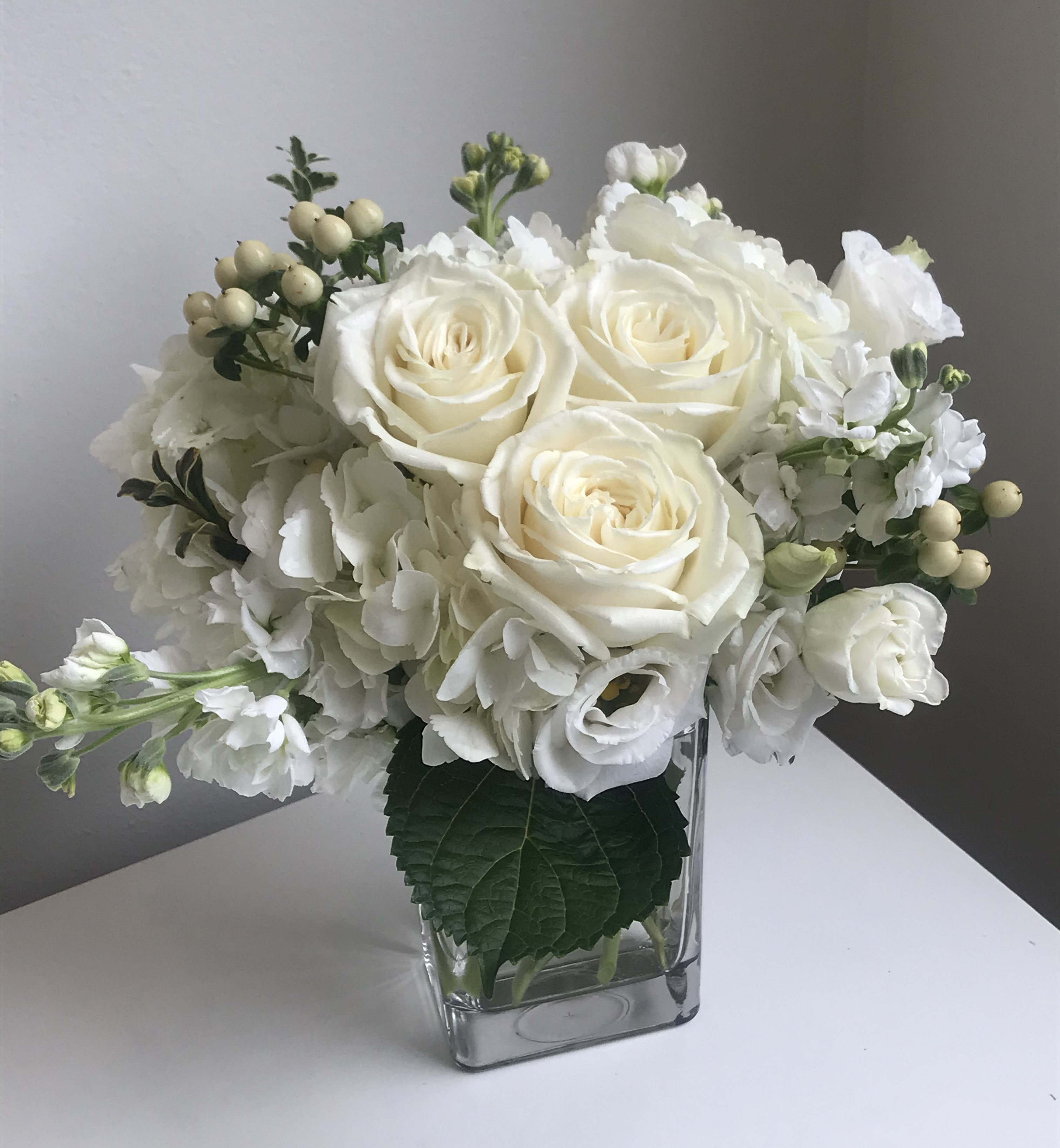 White roses and hydrangeas arranged in a clear square vase