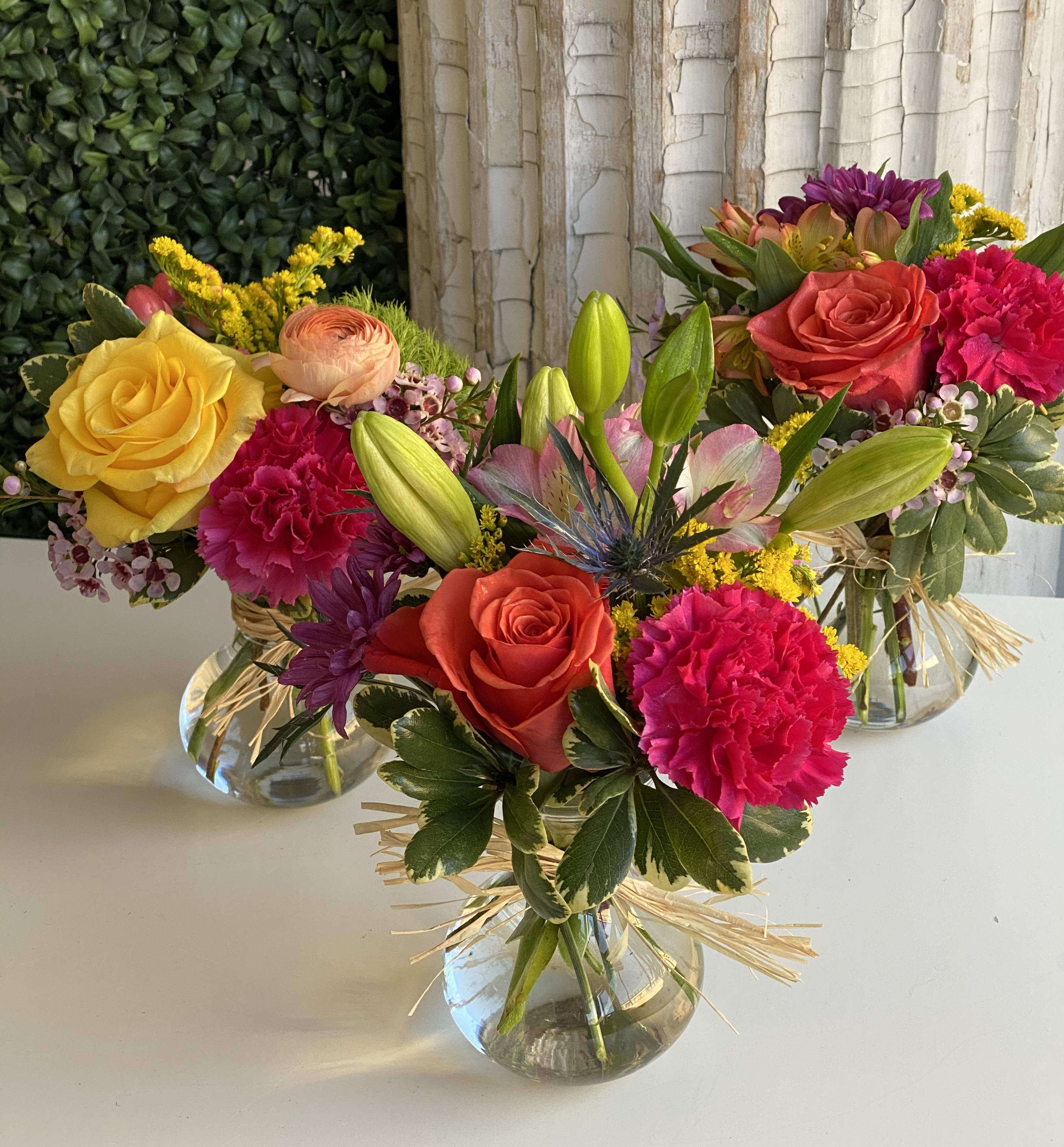Three colorful mixed flower arrangements in clear glass vases
