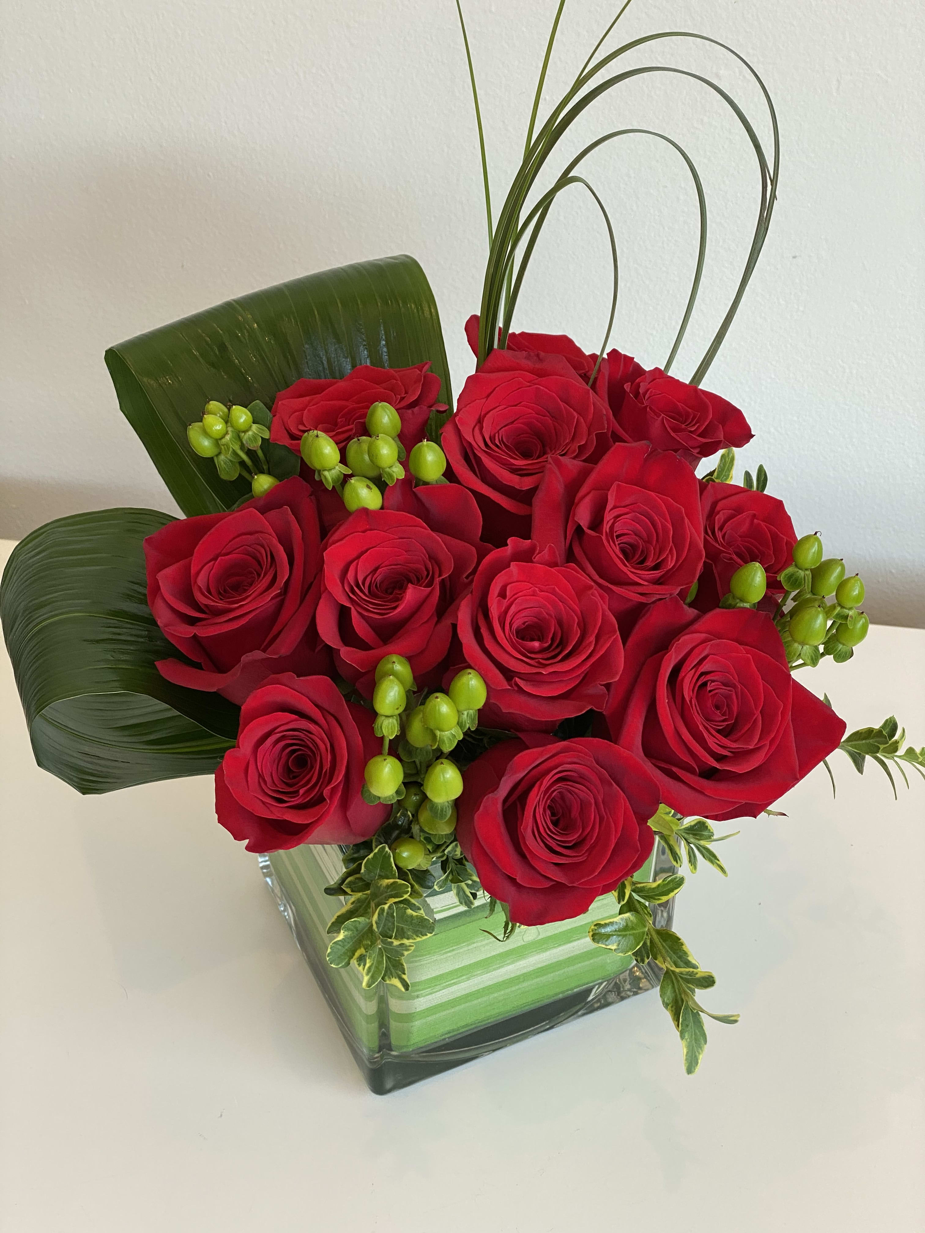 Red roses arranged in a square glass vase with green accents