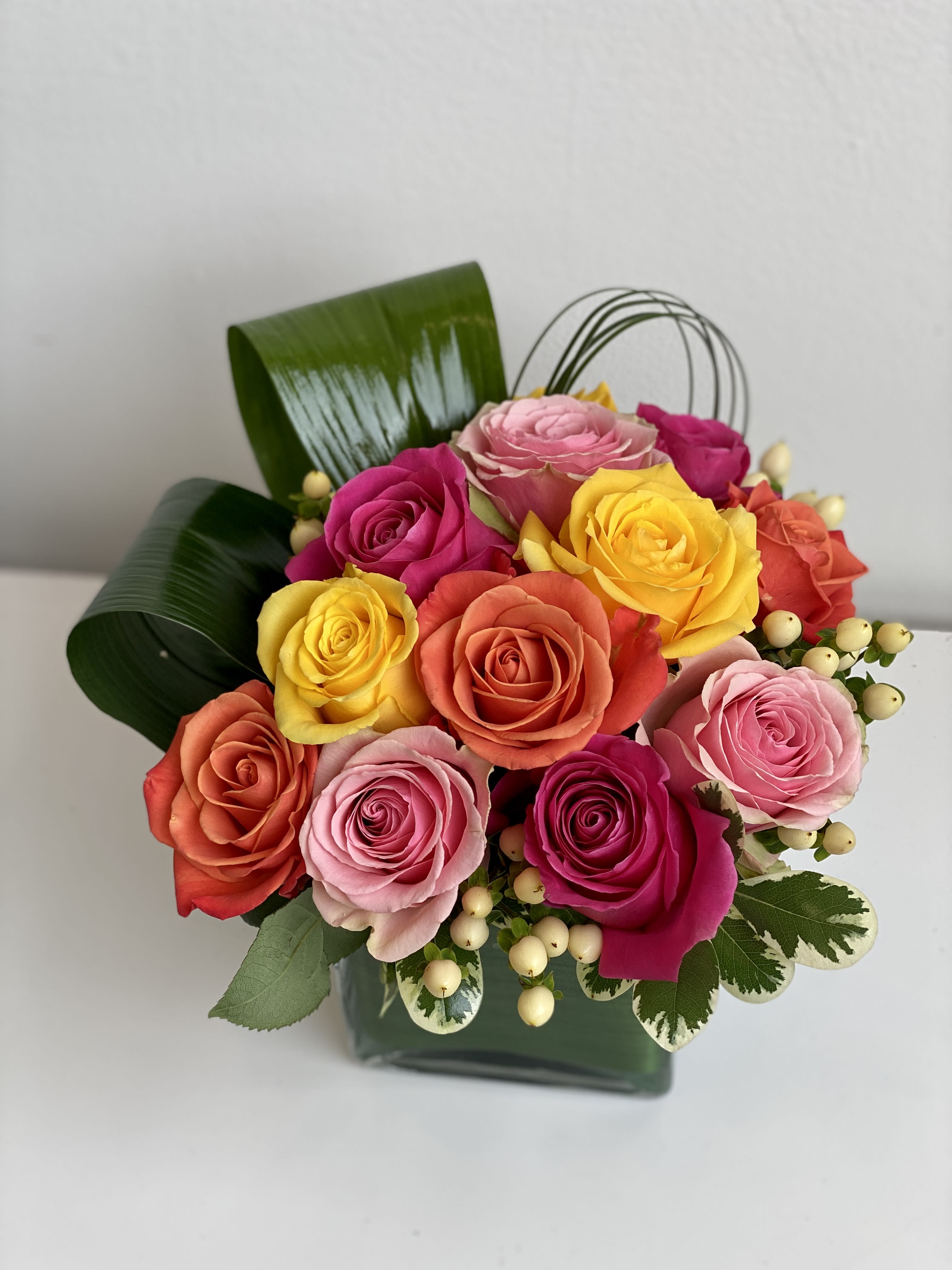 Colorful rose bouquet in a dark green box with decorative leaves