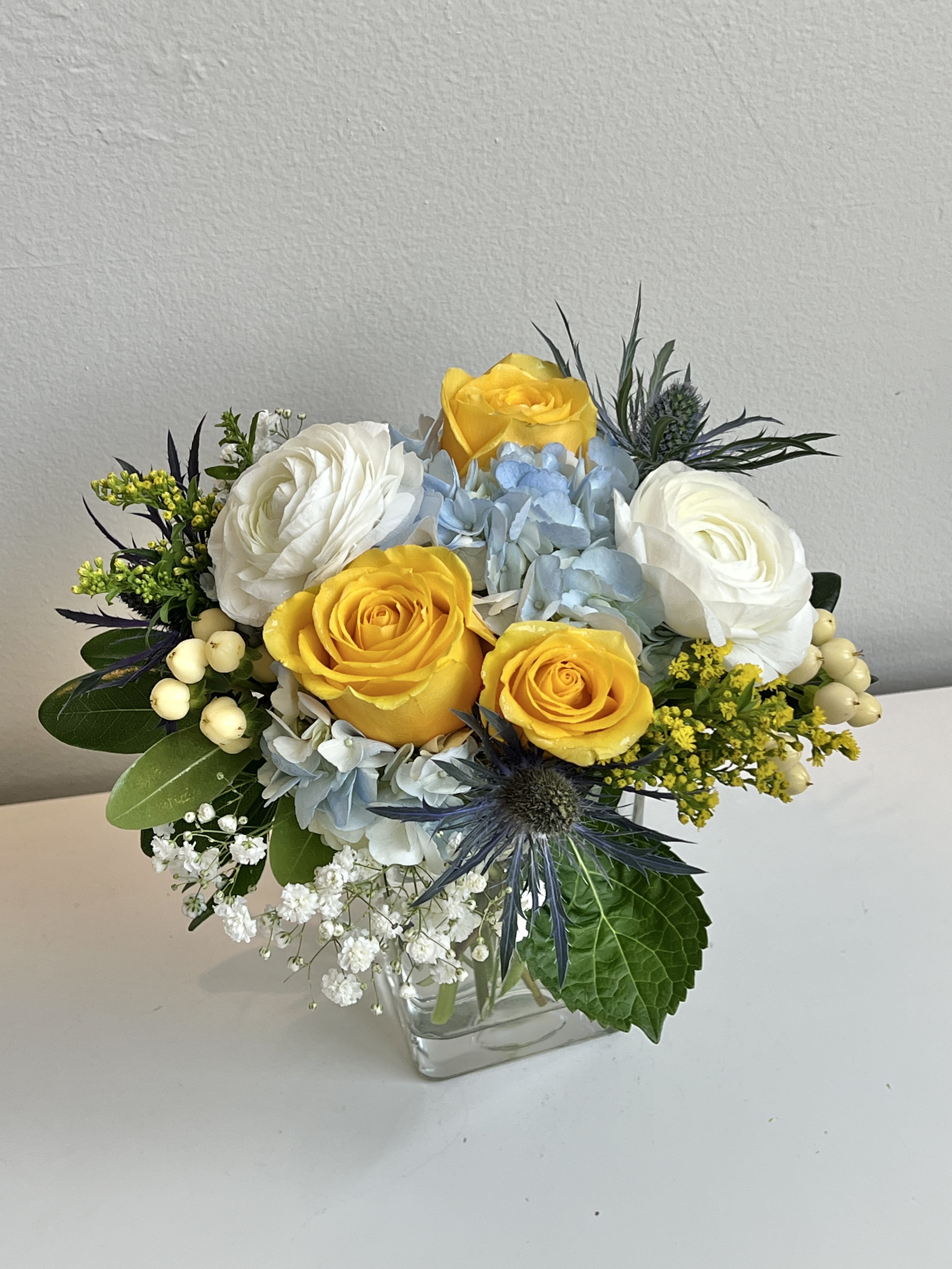 Bouquet of yellow and white roses with blue hydrangeas in a glass vase