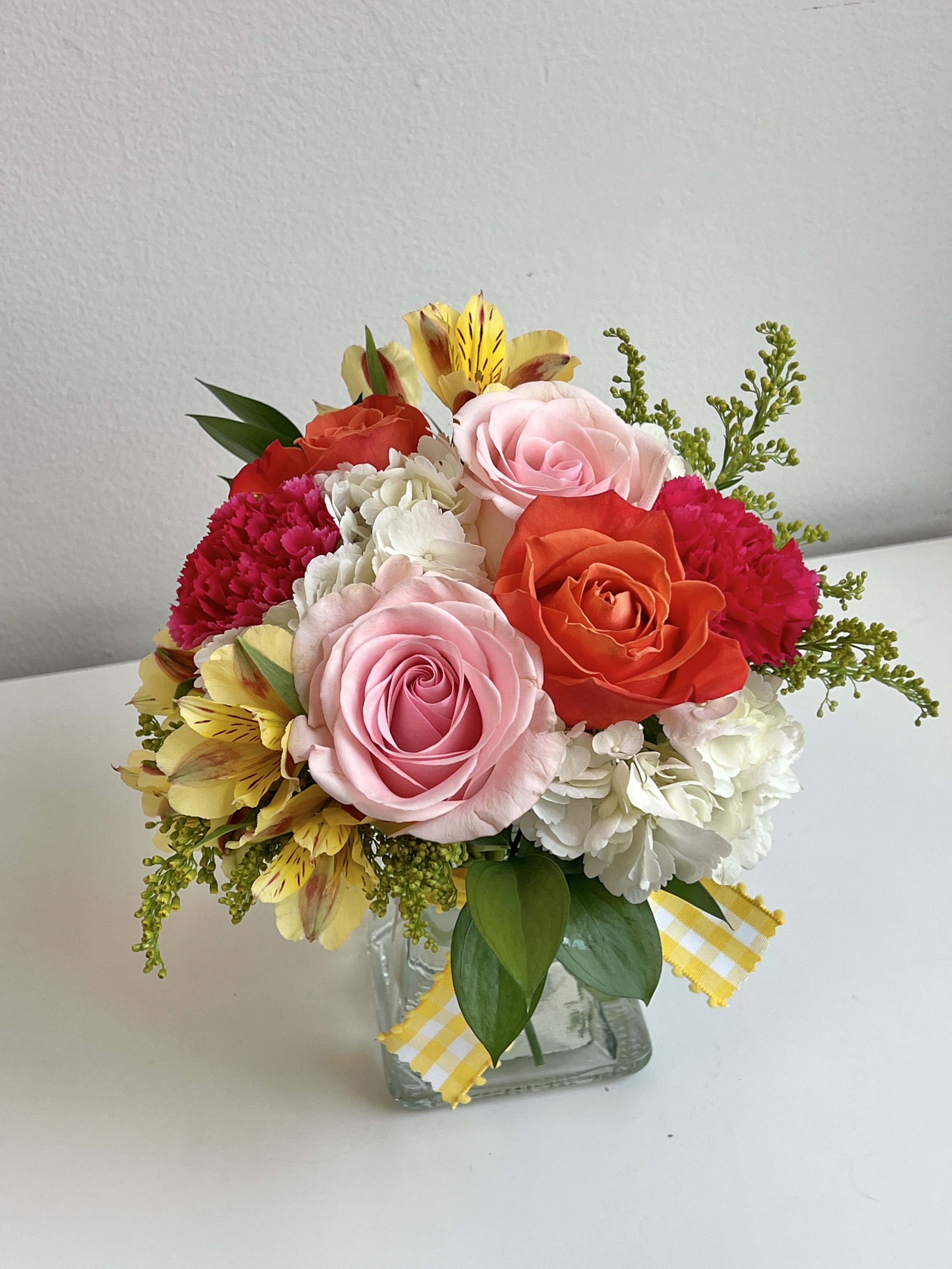 Mixed bouquet of roses, carnations, and white blooms in a glass vase