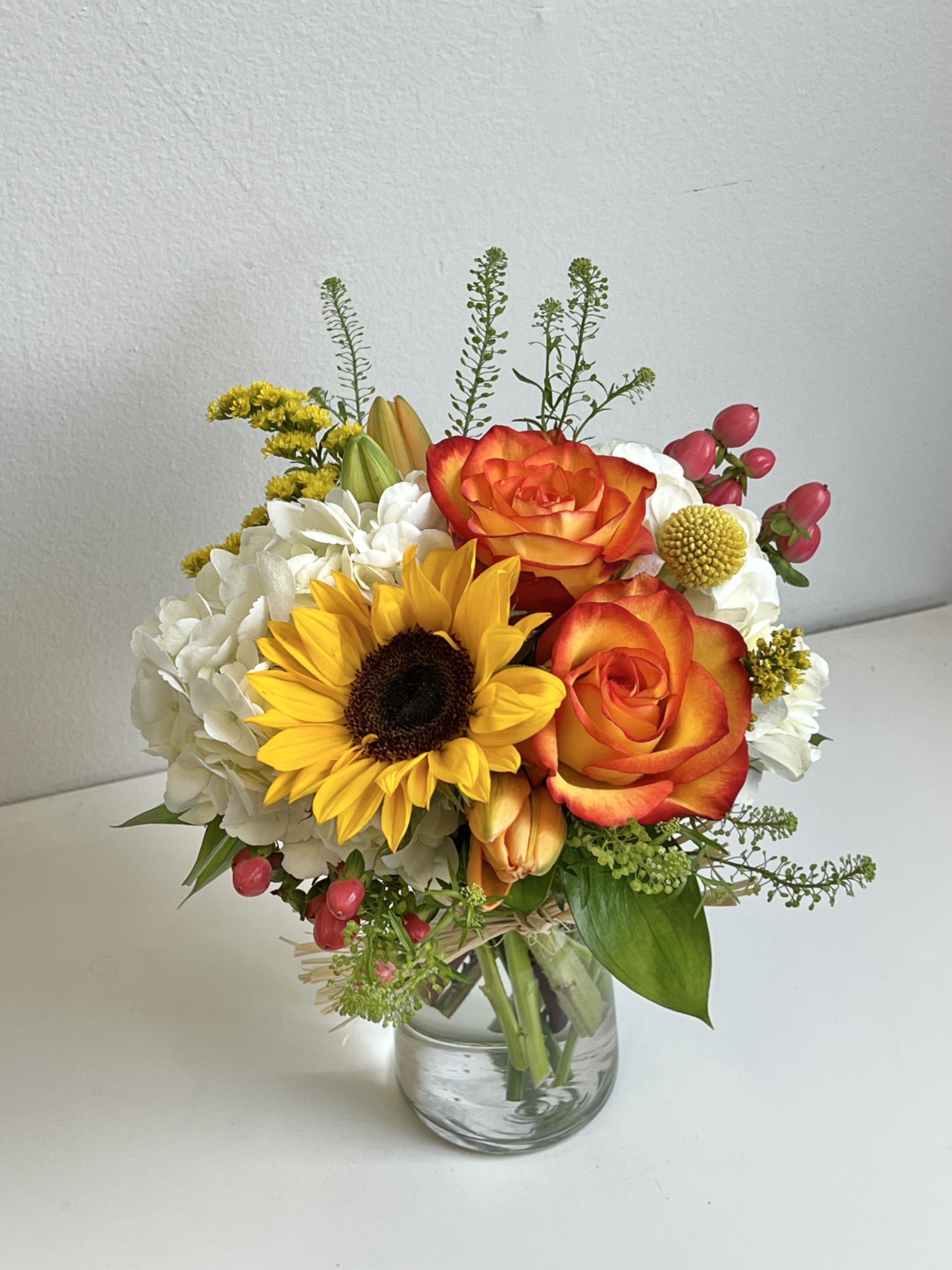 Bouquet of orange roses, a sunflower, and white hydrangeas in a glass vase