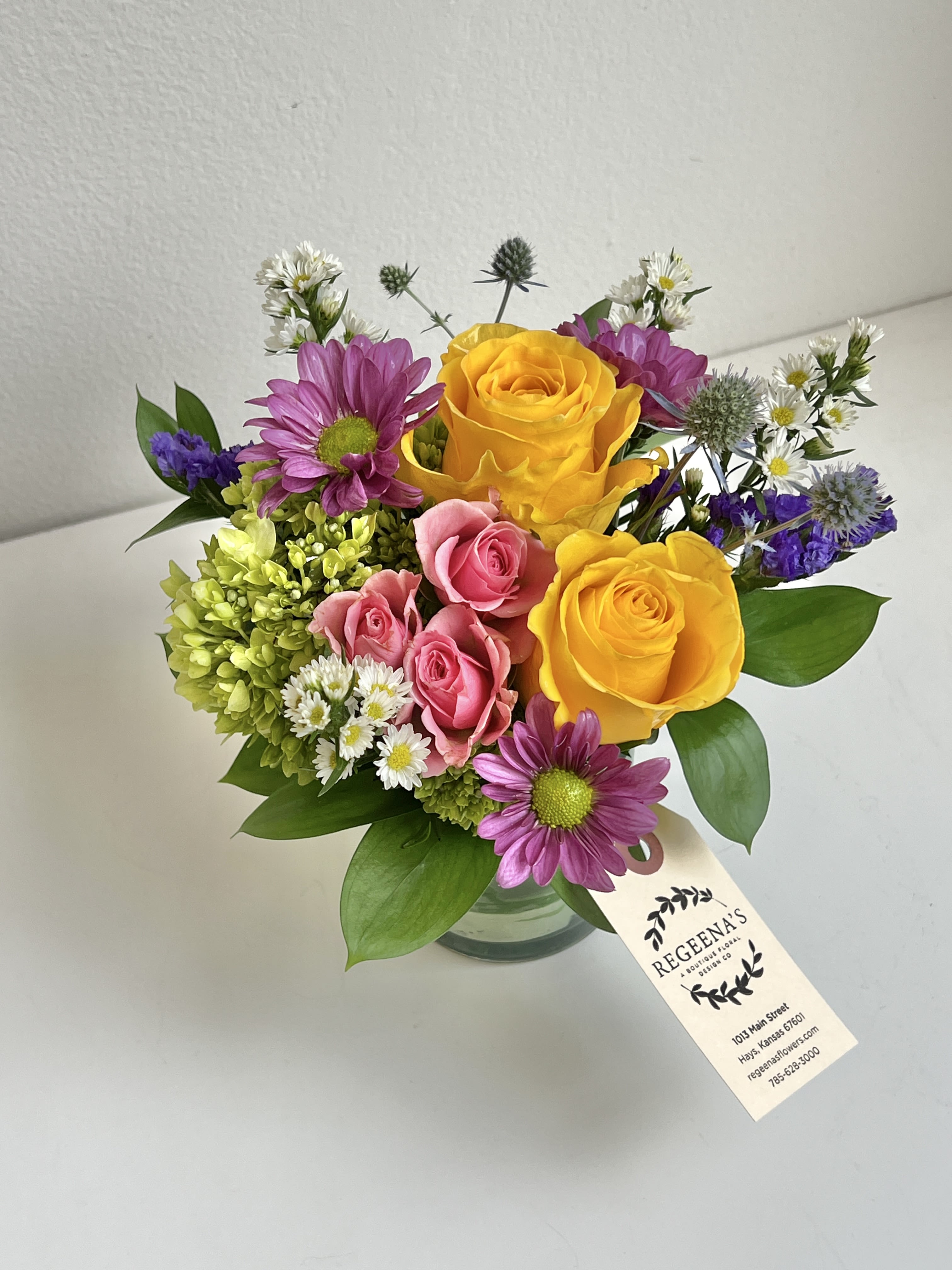 Bouquet of yellow and pink roses with purple daisies in a glass vase