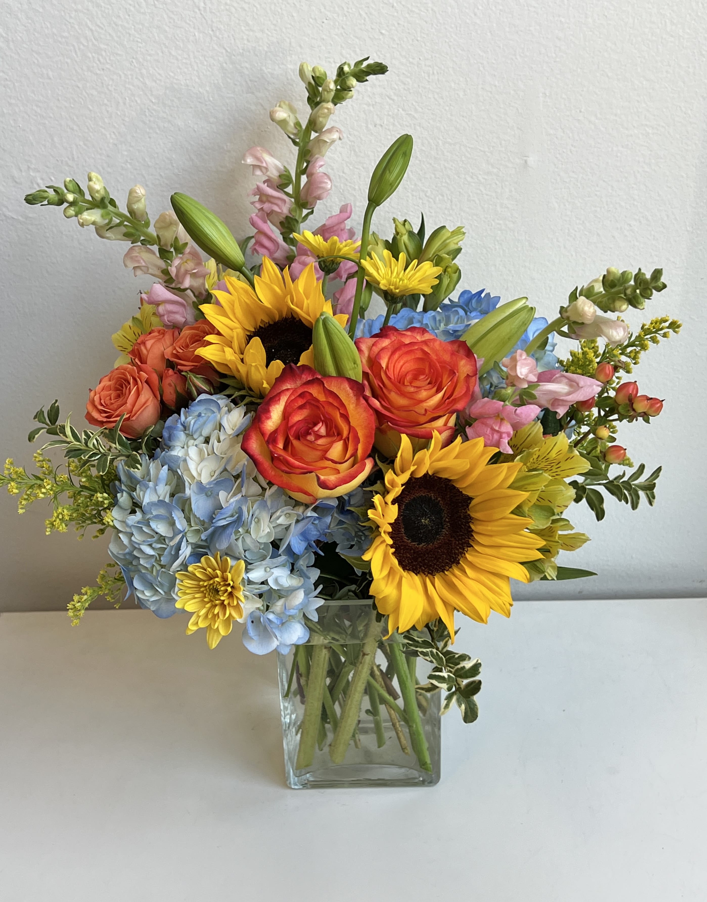 Mixed bouquet with sunflowers, roses, hydrangeas, and snapdragons in a glass vase