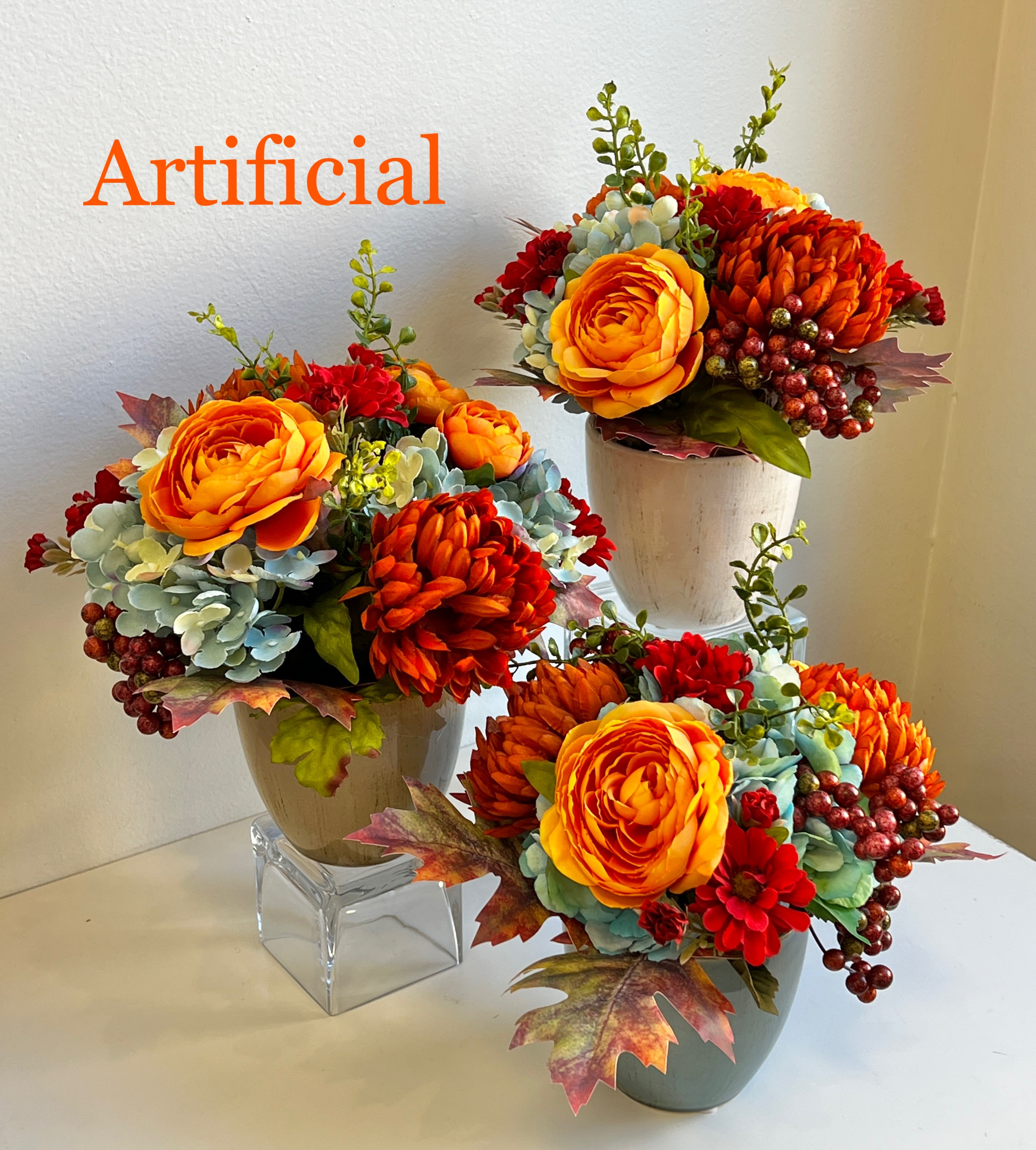 Three artificial floral arrangements in small vases with orange and red blooms