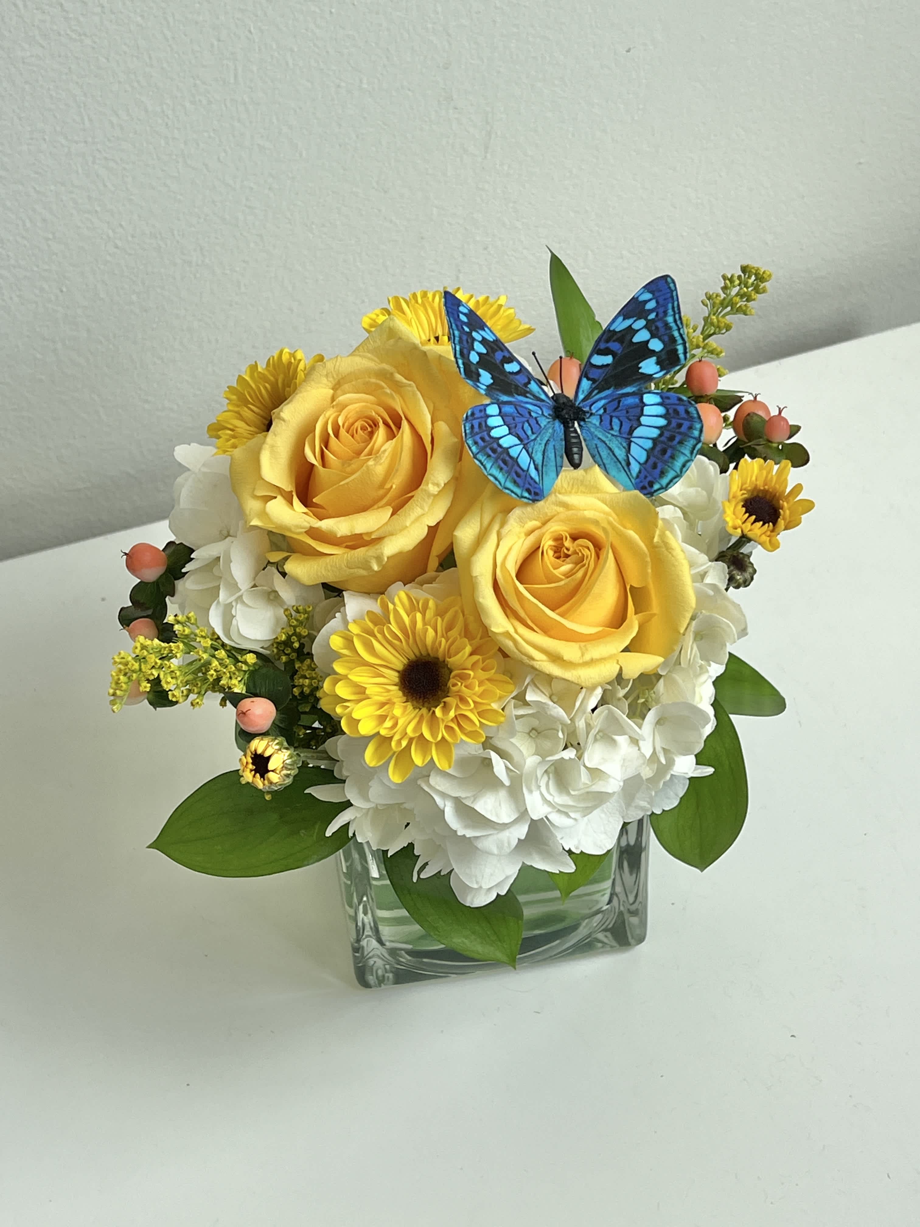 Yellow roses and white hydrangeas in a glass vase with a blue butterfly accent