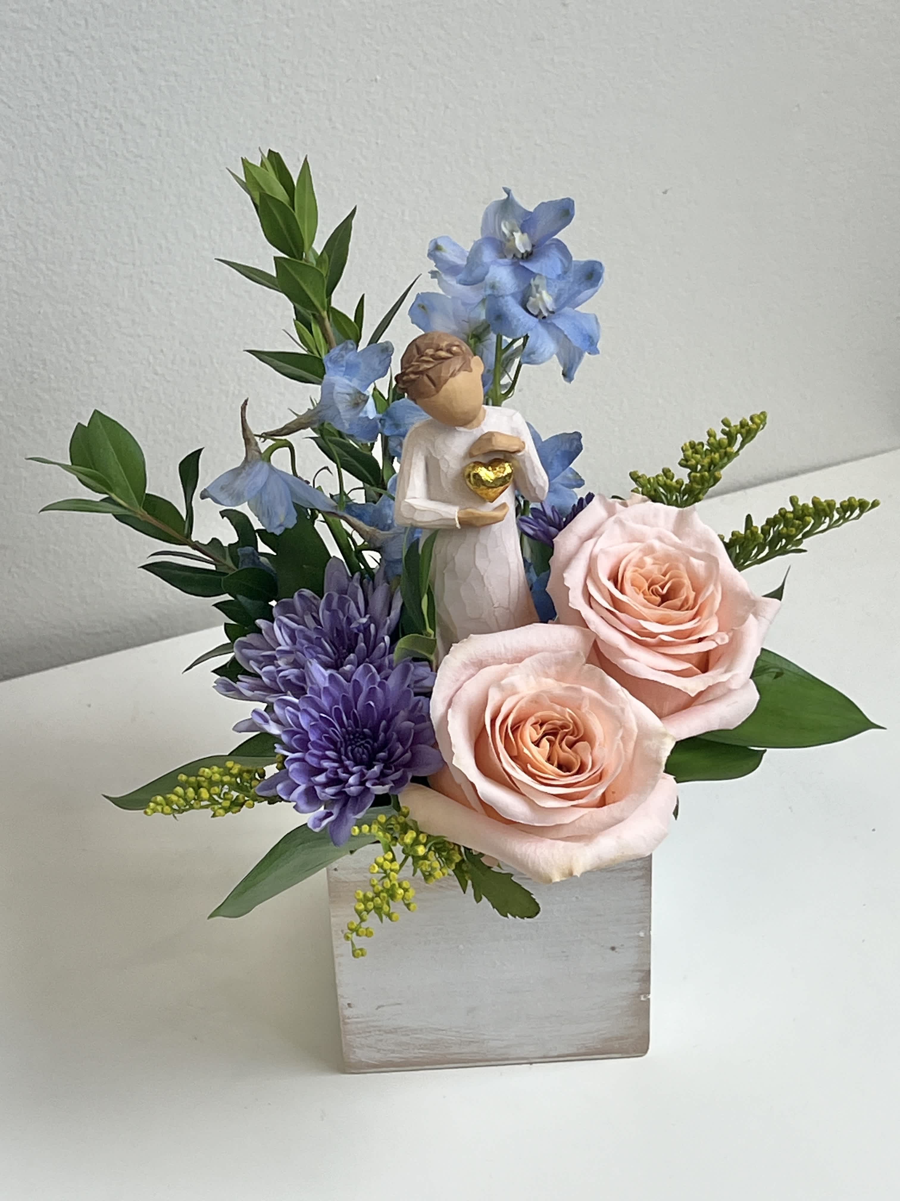 Pink roses and purple flowers in a square vase with a small angel figurine