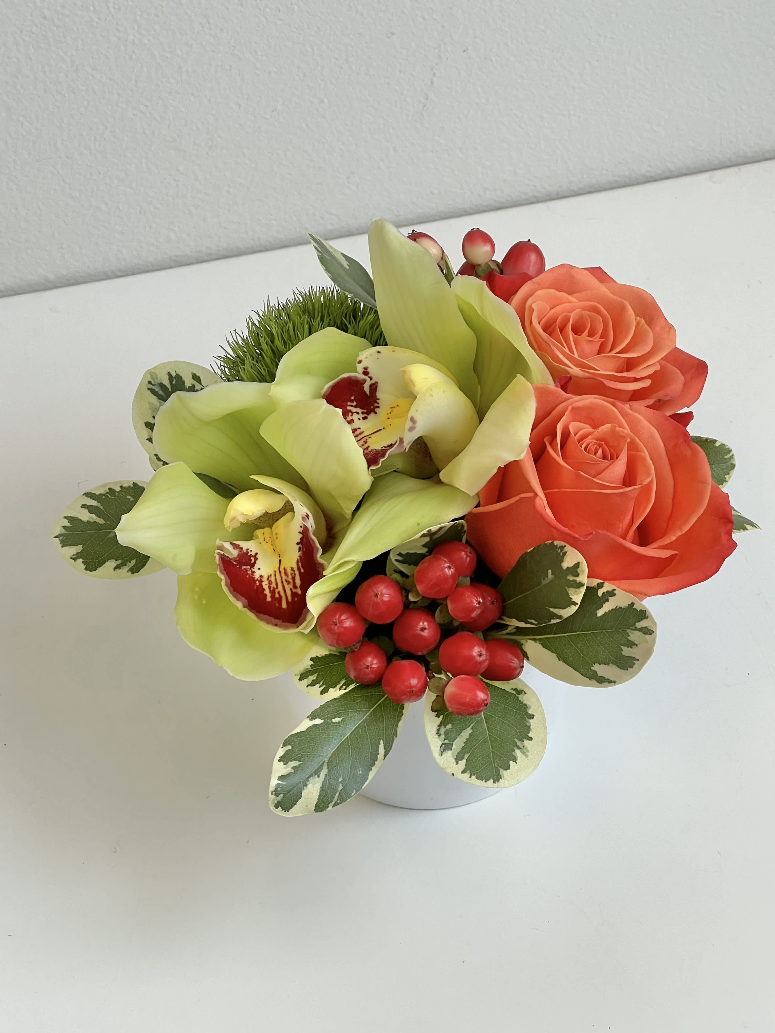 Compact bouquet with orange roses, green orchids, and red berries in a white vase