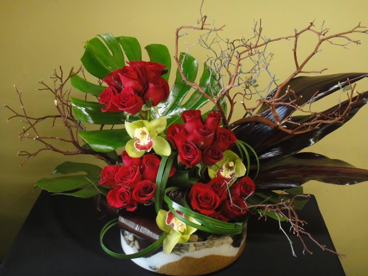 Red roses and yellow orchids arranged in a low container with branches