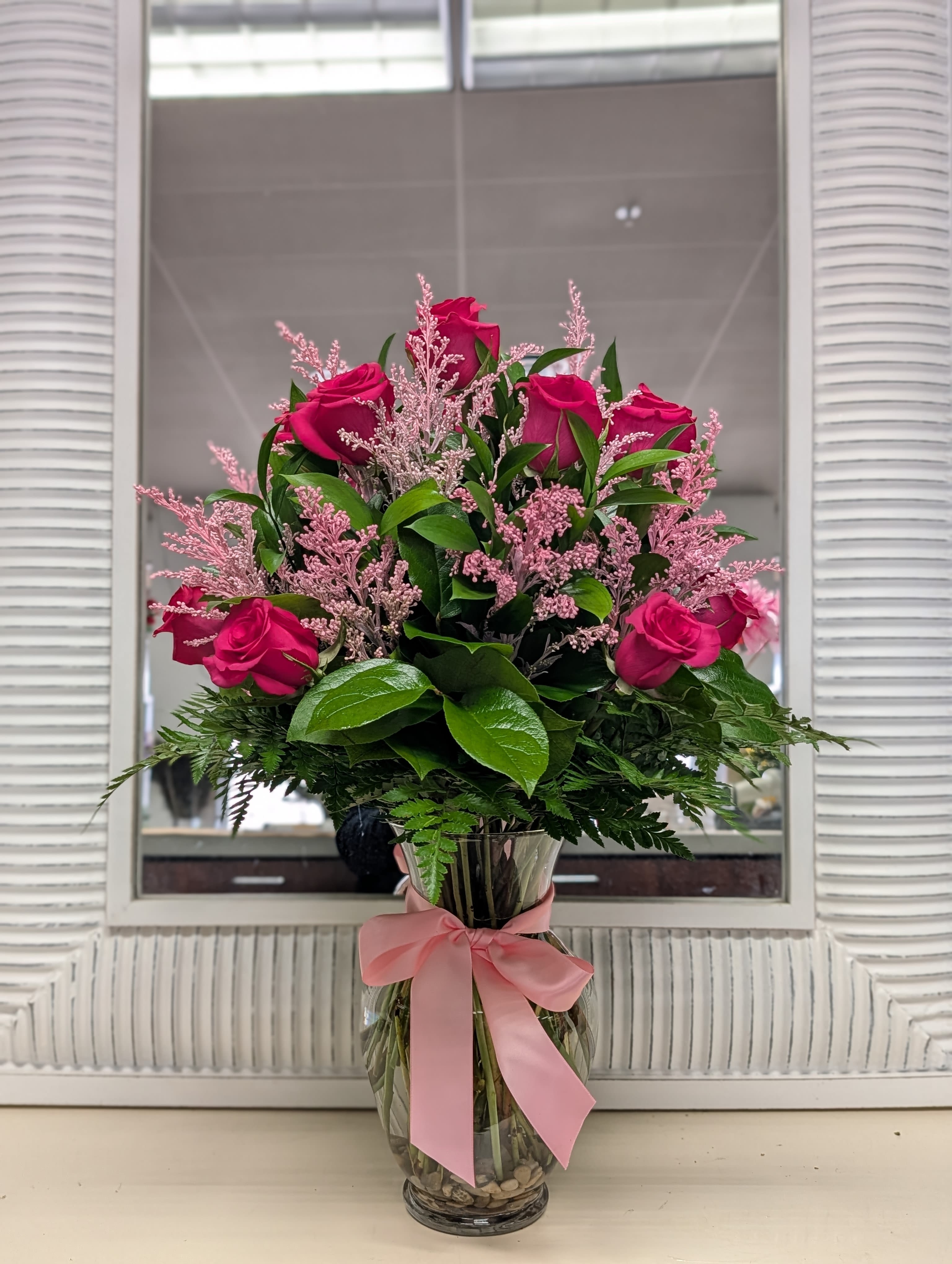 Tall arrangement of hot pink roses with pink filler in a clear glass vase tied with a pink bow.