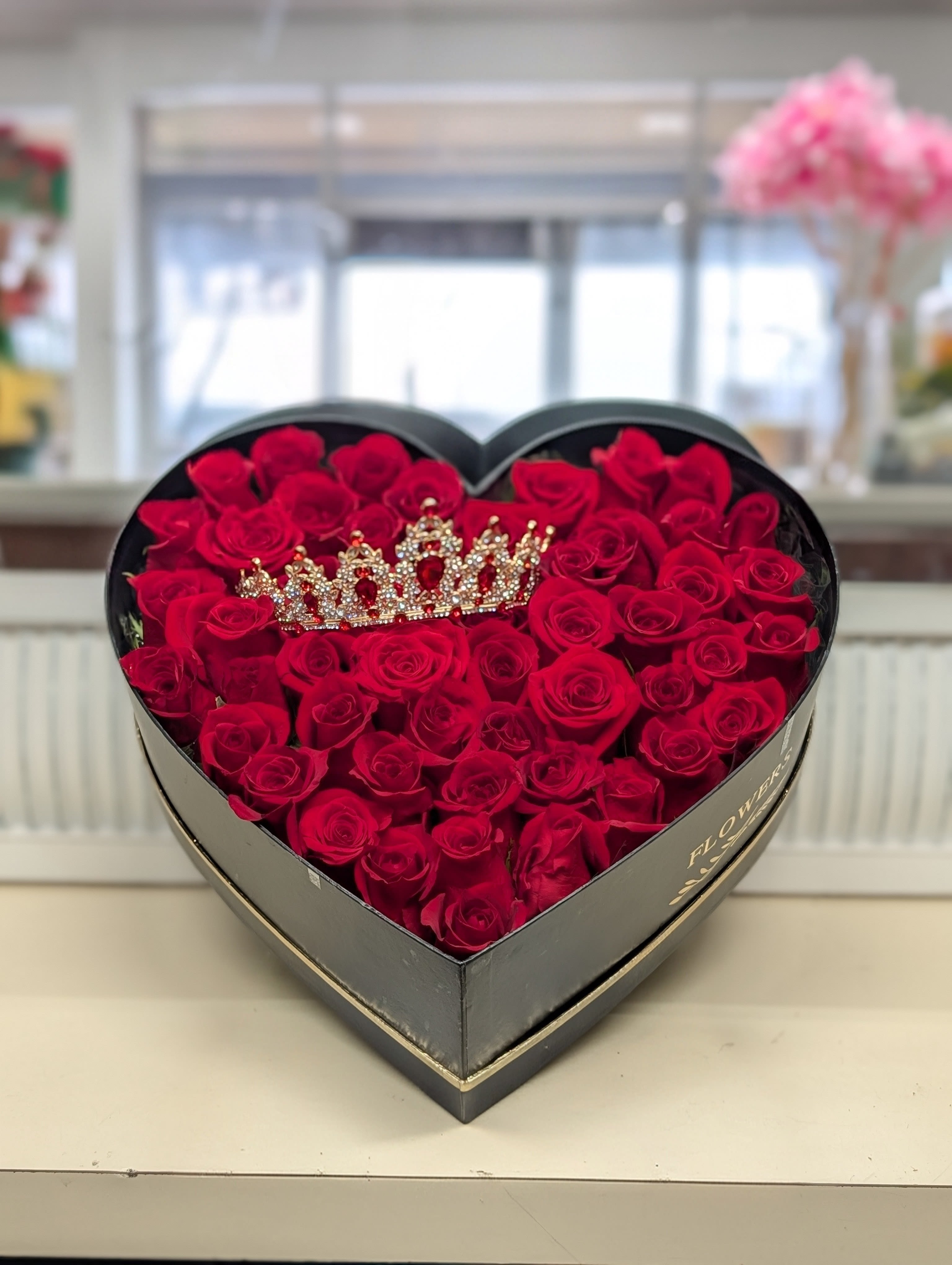Heart-shaped black box filled with red roses and a jeweled crown ornament on top