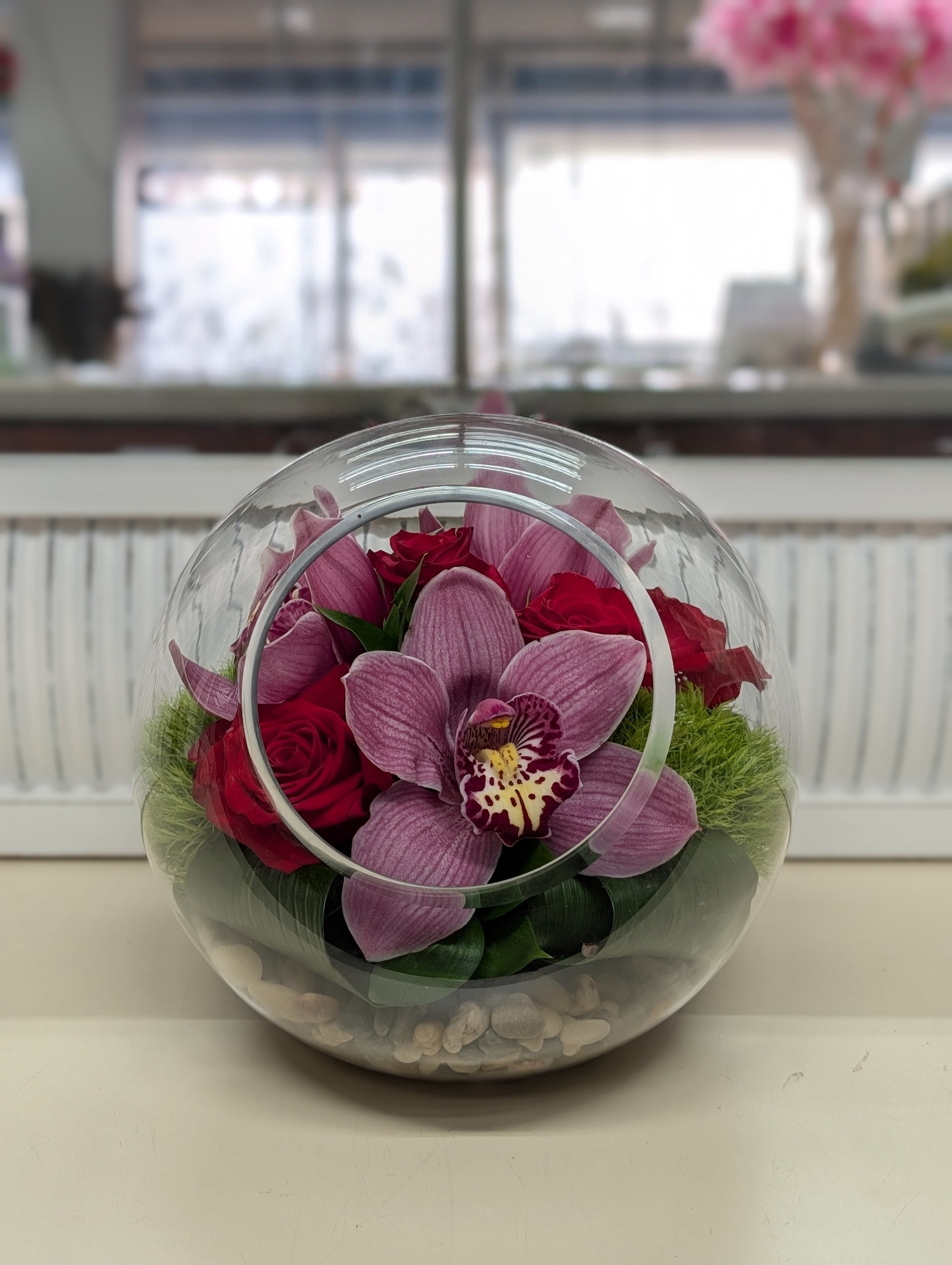 Pink orchids and red roses in a clear round glass vase