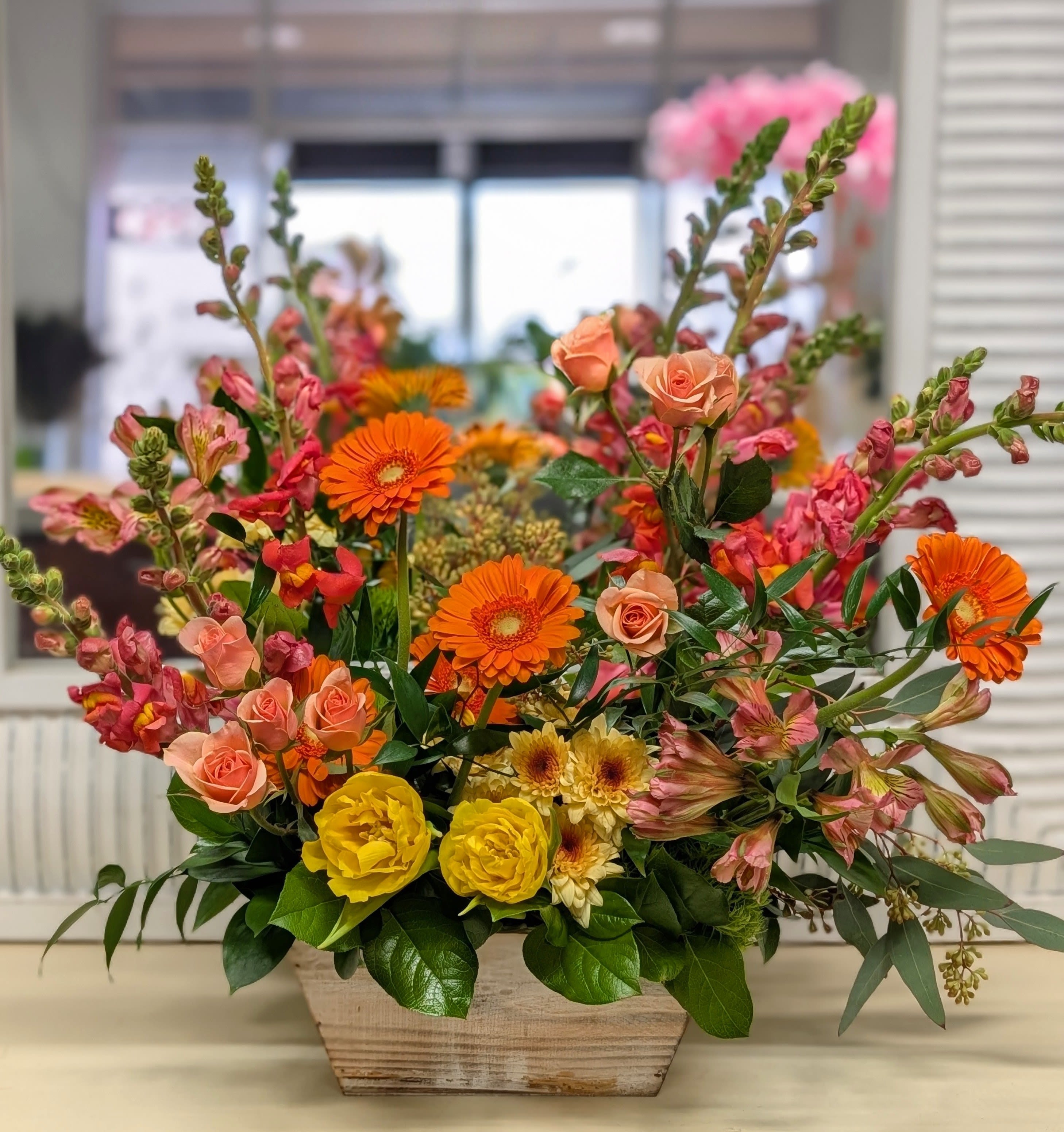 Mixed bouquet in a wooden planter with orange, pink, and yellow flowers
