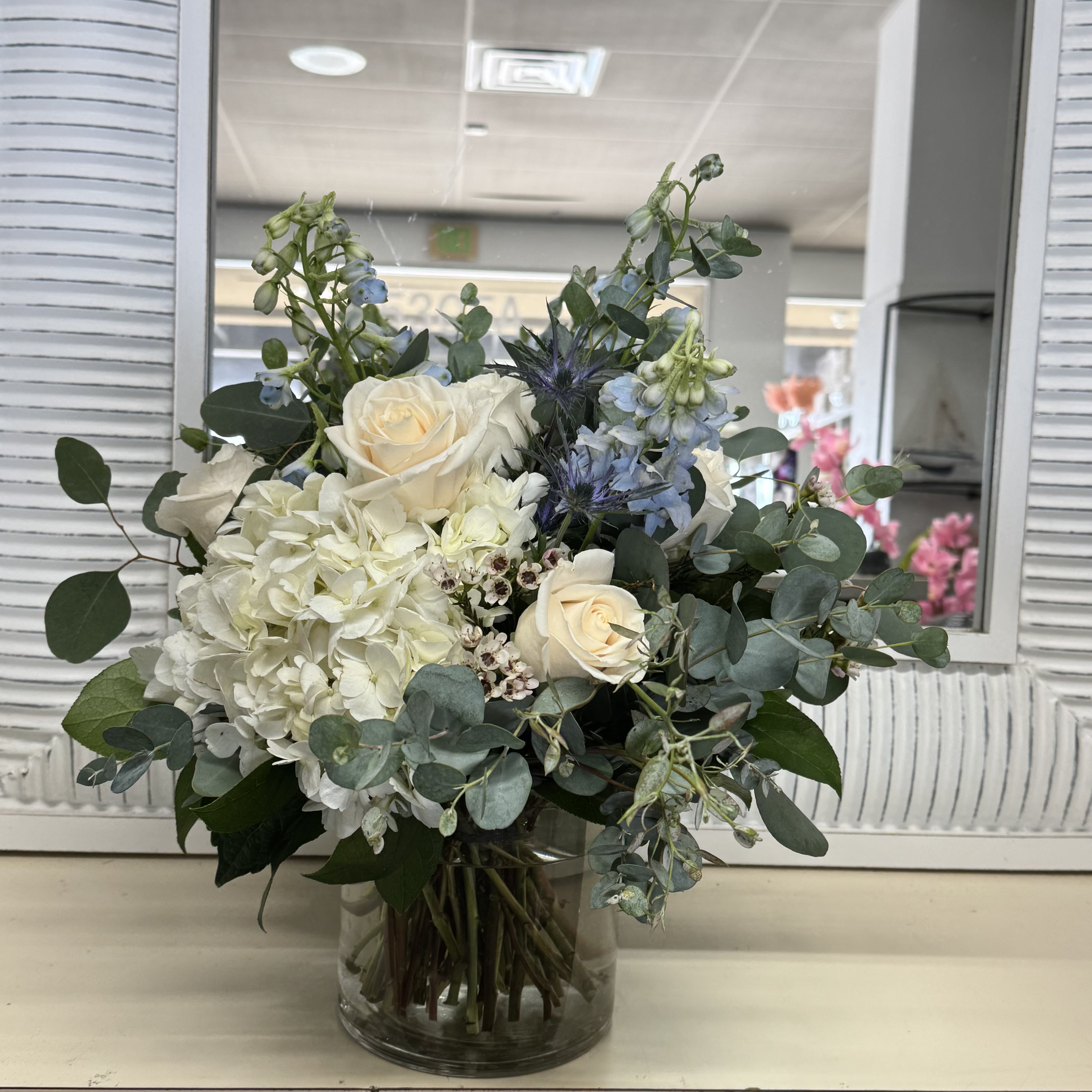 White roses and hydrangea in a glass vase with blue flowers and eucalyptus