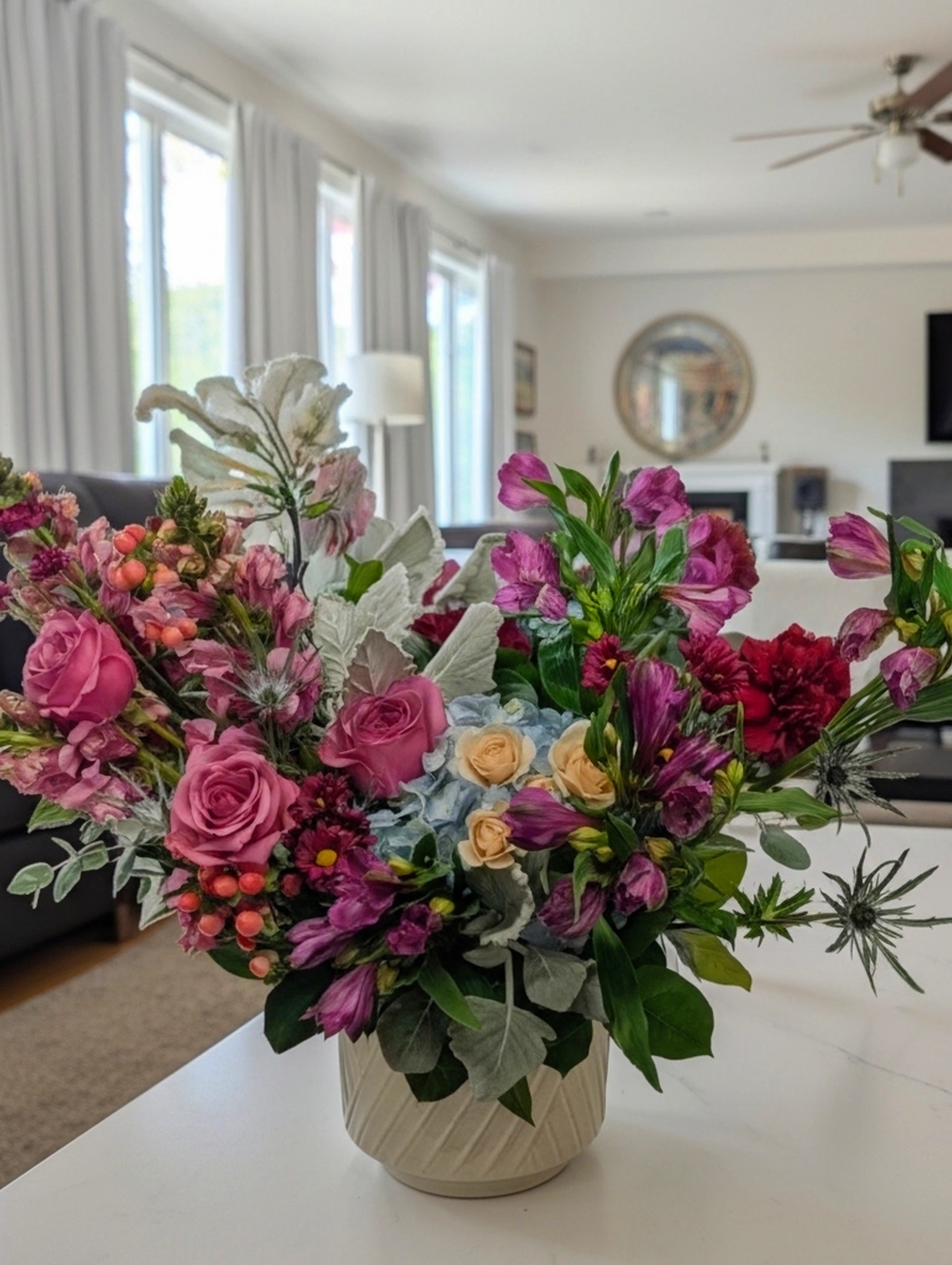 Mixed bouquet of pink and purple flowers in a cream vase