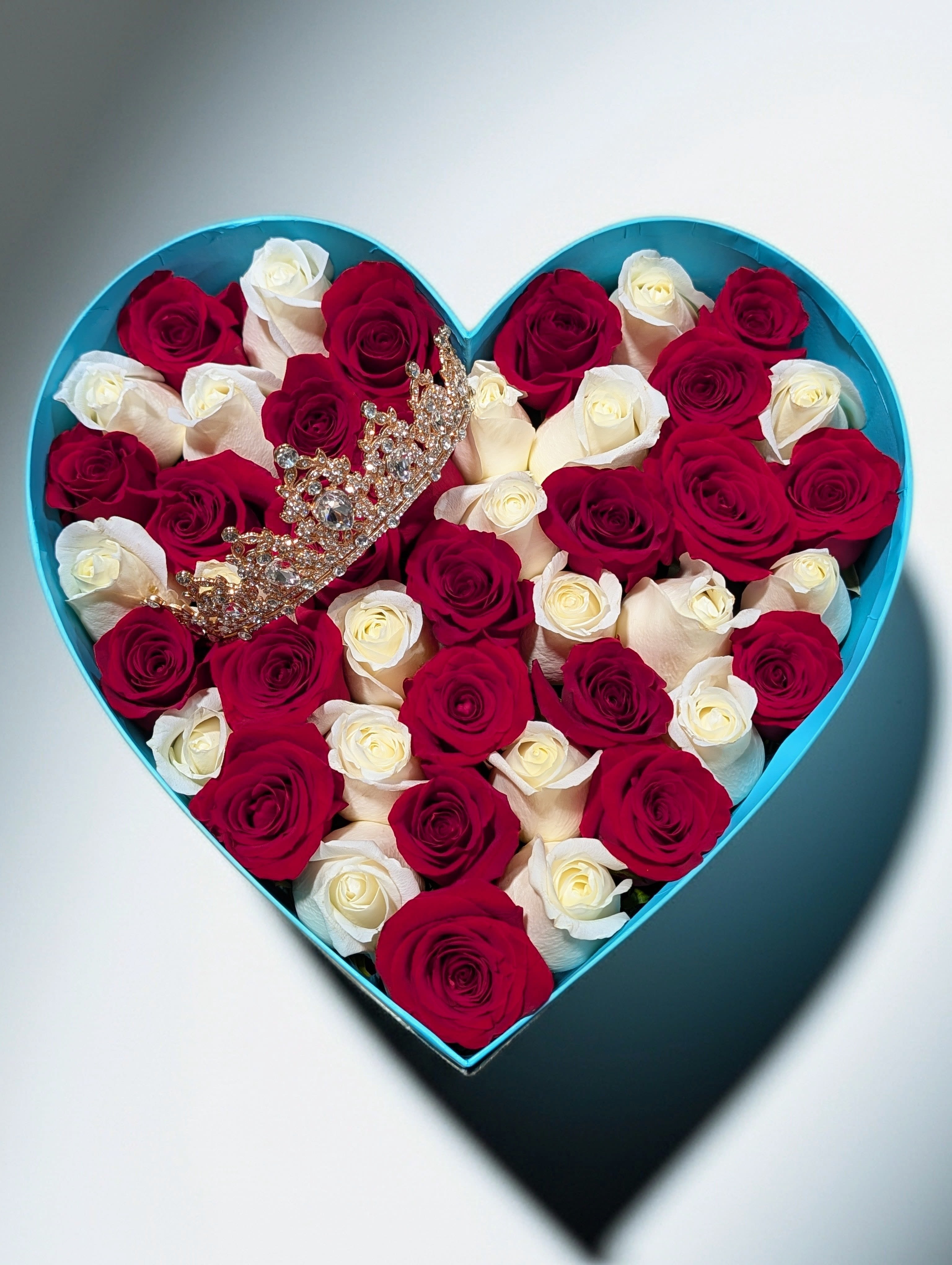 Heart-shaped turquoise box filled with red and white roses with a jeweled crown on top