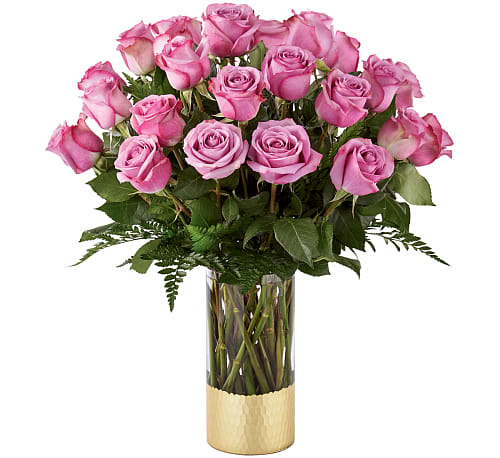 Pink roses arranged in a tall glass vase with a gold base