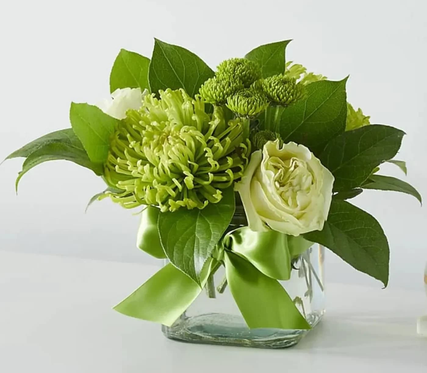 Green and white floral arrangement in a clear glass vase with a ribbon