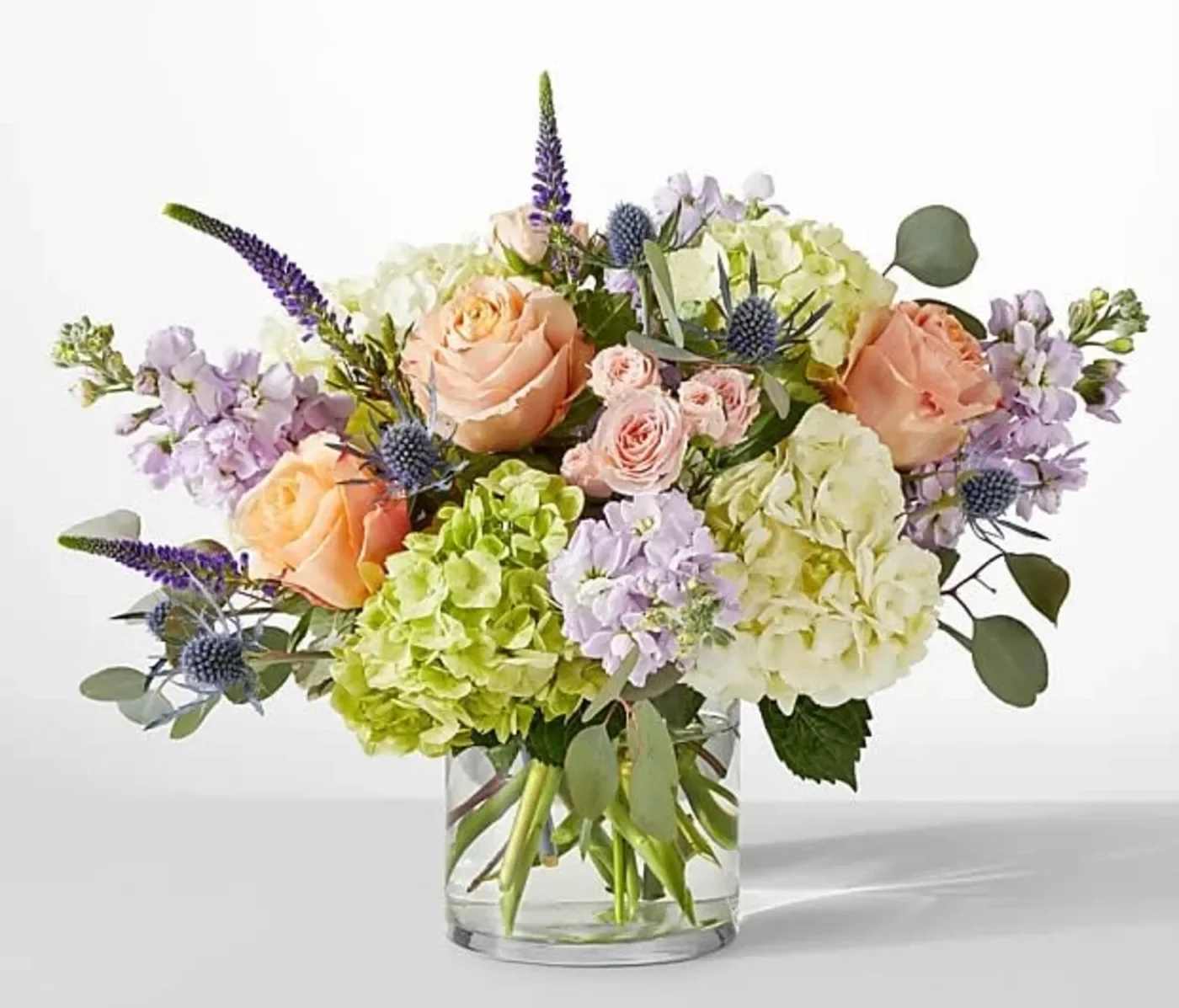 Bouquet of peach roses, hydrangeas, and purple flowers in a glass vase
